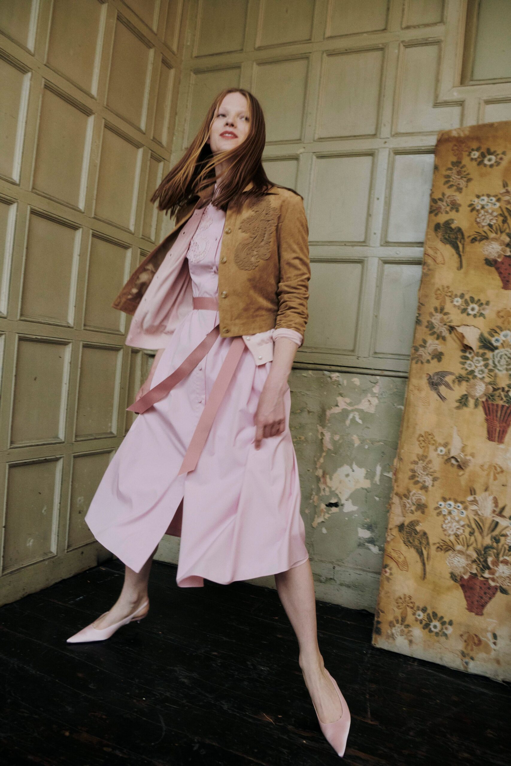 Cropped tan suede jacket with tonal floral cutwork curling over one chest. Powder-pink shirtdress with a lace bib and long grosgrain ties. Pale pink pointed slingbacks. Crossing a creaky drawing room before tea is poured.