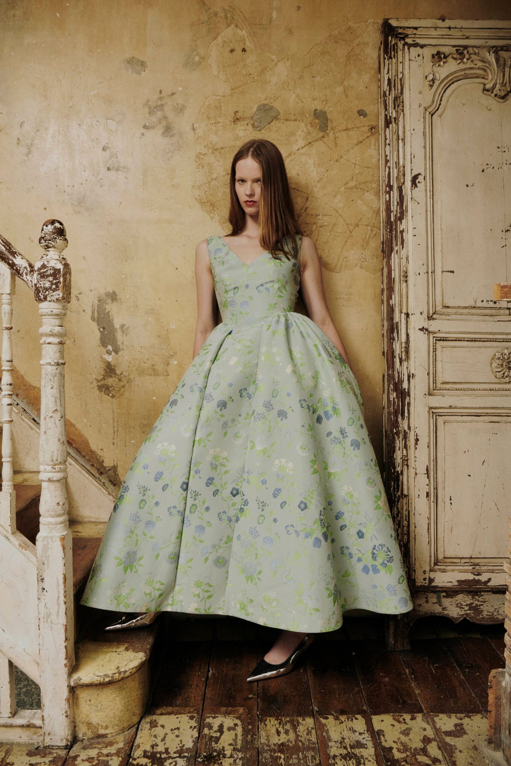 Pale celadon jacquard ball dress, blue floral brocade and deep box pleats. Black pumps with sharp silver cap toes. Standing in a peeling villa hallway before the house is opened for spring.