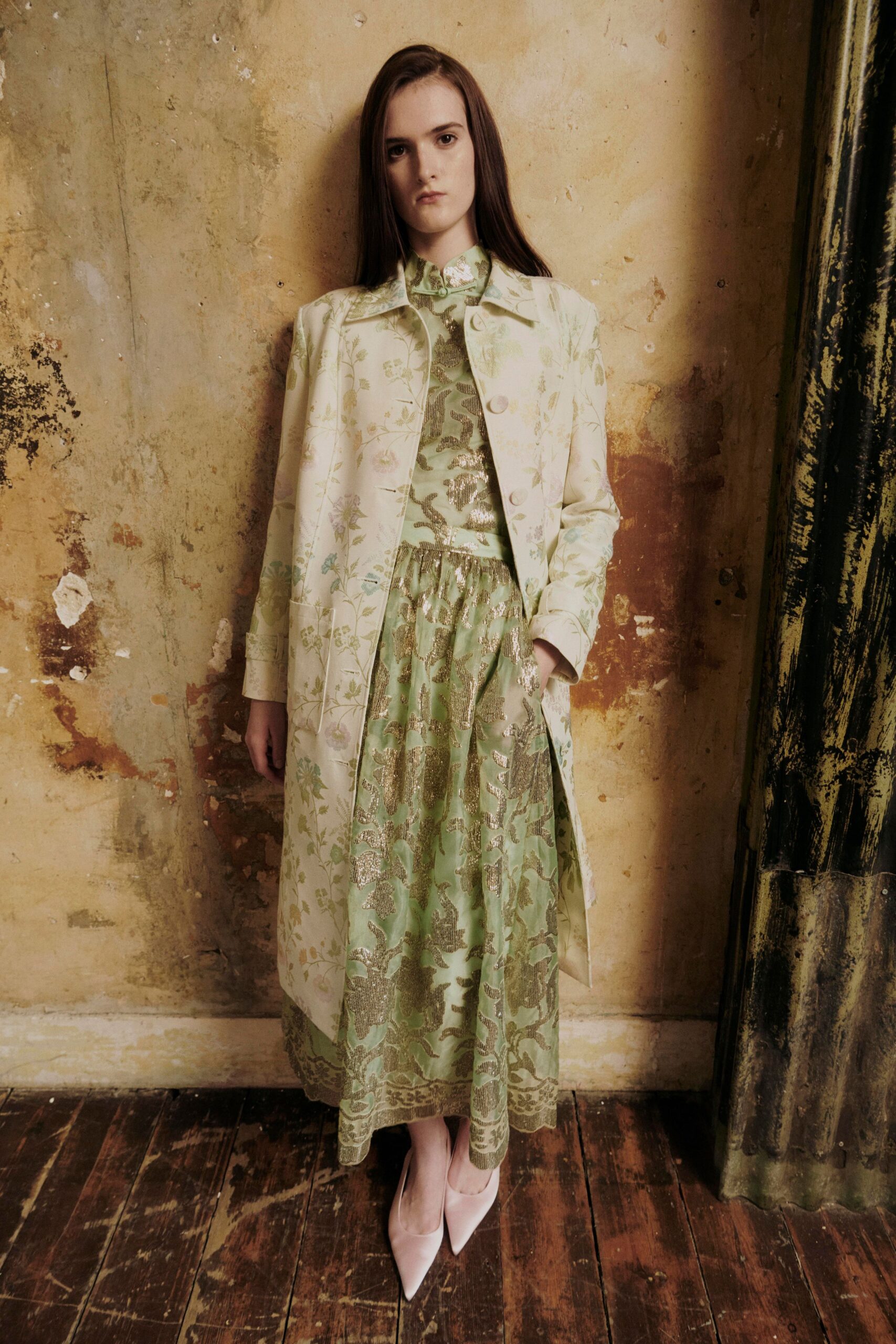 Ivory floral brocade coat with oversized covered buttons and cuff tabs. Mint fil coupe dress, metallic vine motifs over a gathered drop waist. Pale blush pointed pumps. Afternoon in a faded hotel salon, wallpaper lifting near the radiator.