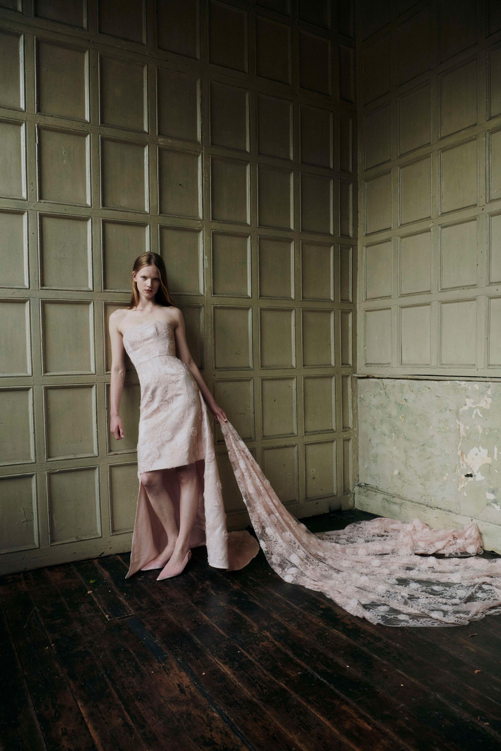Blush strapless brocade gown, knee-length front cut to a sweeping lace train. Pale pink pointed pumps. After the ceremony, alone in a paneled room with splintered floorboards.