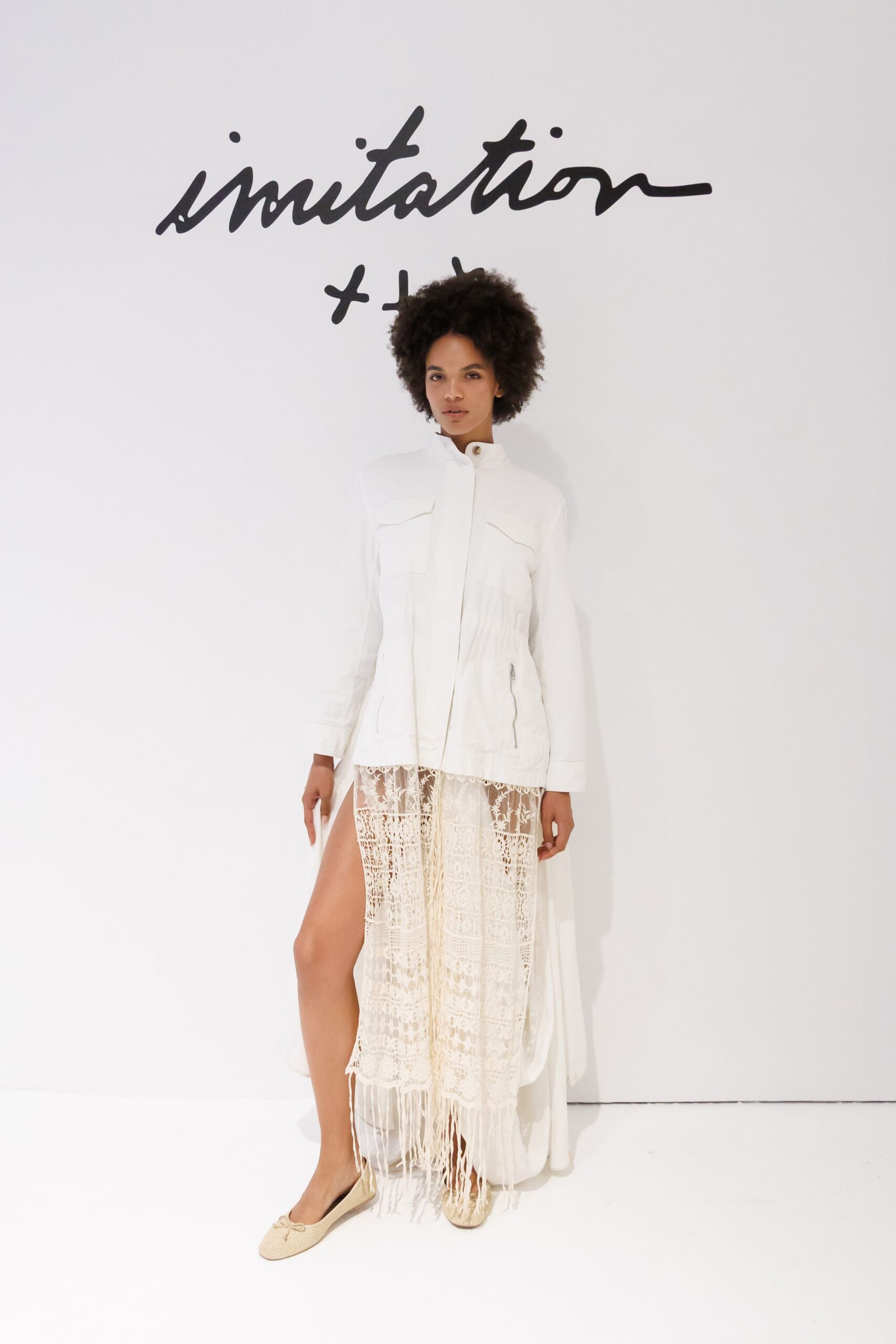 White utility jacket with a stand collar and curved flap pockets. Ivory crochet lace skirt, thigh slit opening under a gauzy overskirt. Cream woven ballet flats with tiny bow knots. For crossing a hotel courtyard barefoot-minded after the pool has closed.