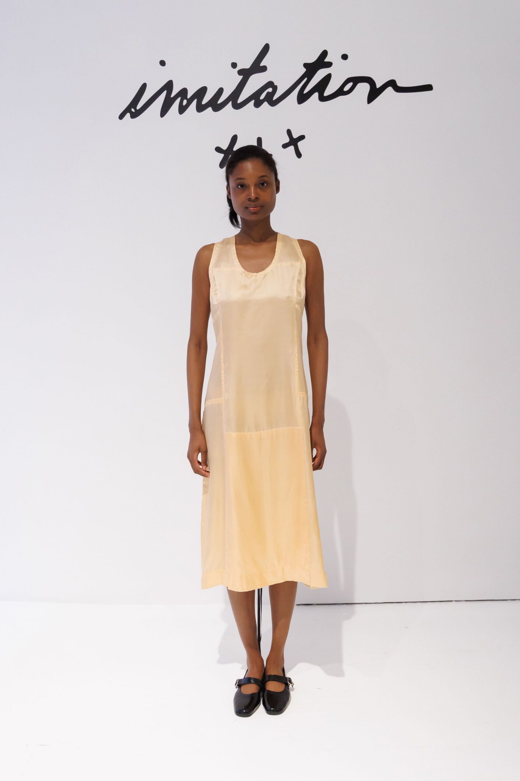 Buttercream satin slip dress with inset panels and a low dropped seam. Black leather Mary Janes with square toes and silver side buckles. Sunday museum hush, reading every wall label in order.