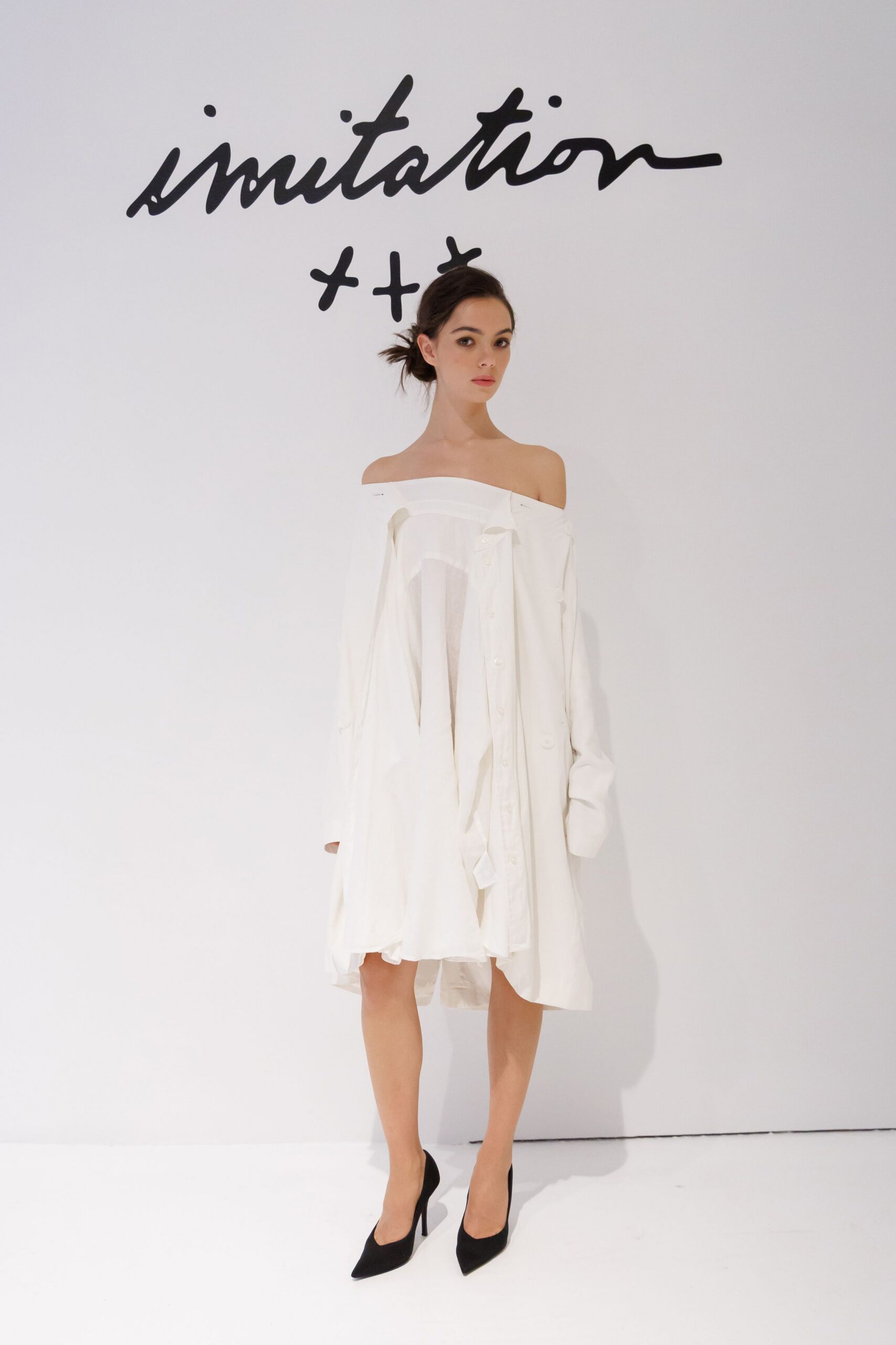 Oversized white shirting worn off the shoulders, placket hanging askew. Gauzy inner layer visible through the open front. Black suede pumps with narrow pointed toes. After the courthouse ceremony, still barefoot in the hotel room except for heels.