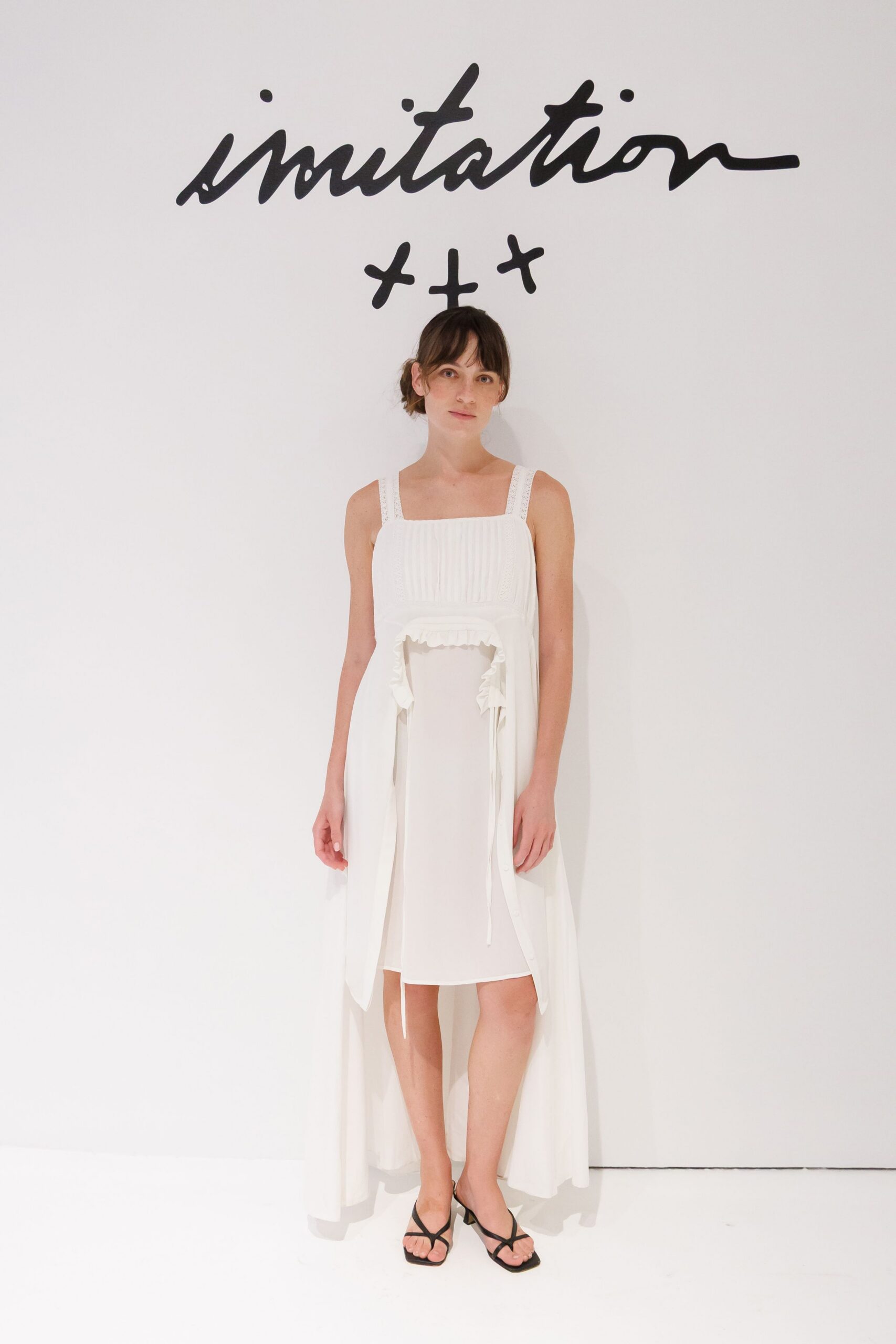 White square-neck dress with pintucked bodice and a ruffled cutout overskirt. Black thong sandals on a low flared heel. City hall at noon, carrying your shoes home in a paper bag.