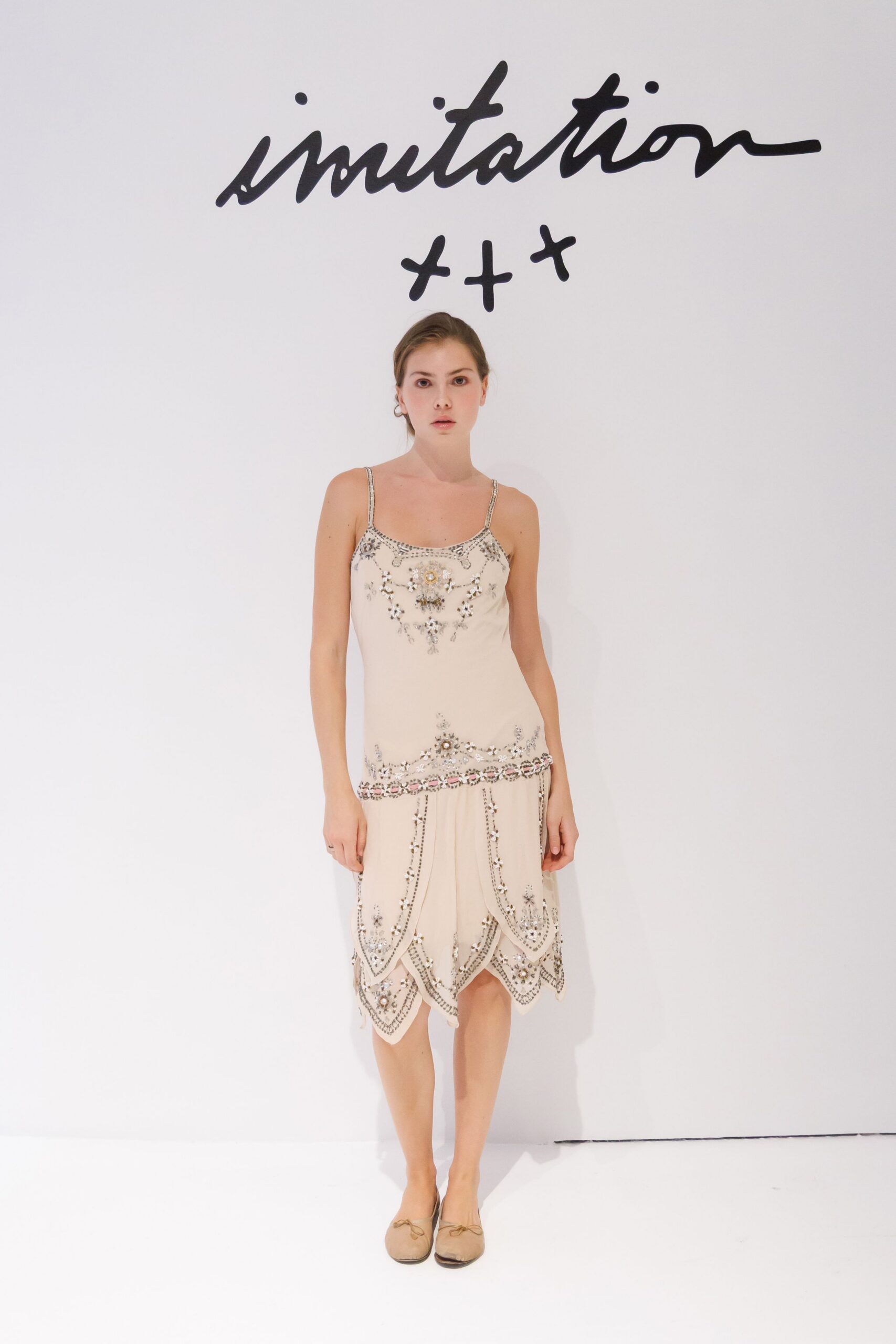Cream slip dress densely beaded with mirrored floral motifs and scalloped godet panels. Nude leather ballet flats with tiny bow knots and darkened toe caps. Afternoon wedding in a town hall with terrazzo floors and weak heating.