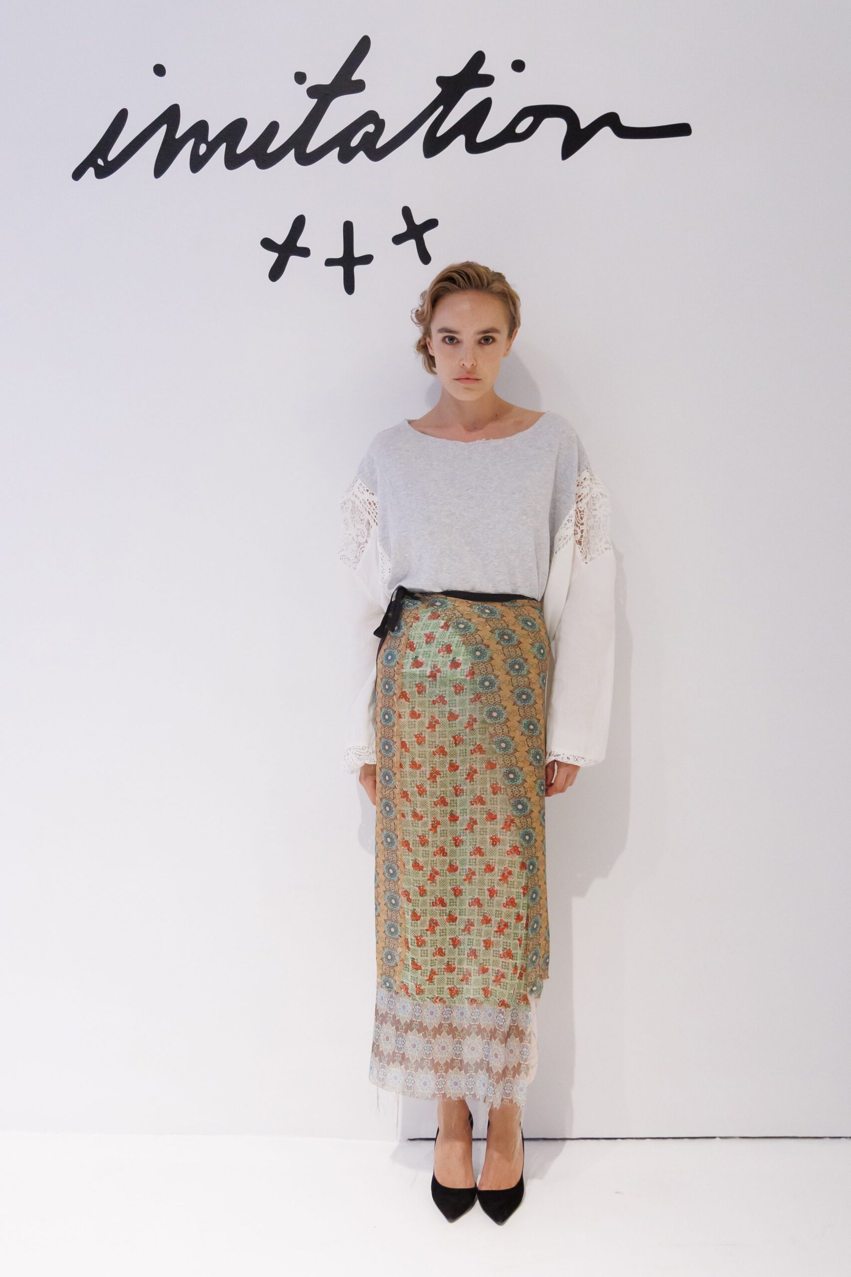 Pale grey jersey top with crochet lace sleeves and a raw boatneck. Column skirt in tapestry jacquard, turquoise medallions framing tiny red sprigs. Black suede pointed pumps. Afternoon in a borrowed apartment, flowers wilting beside the fruit bowl.