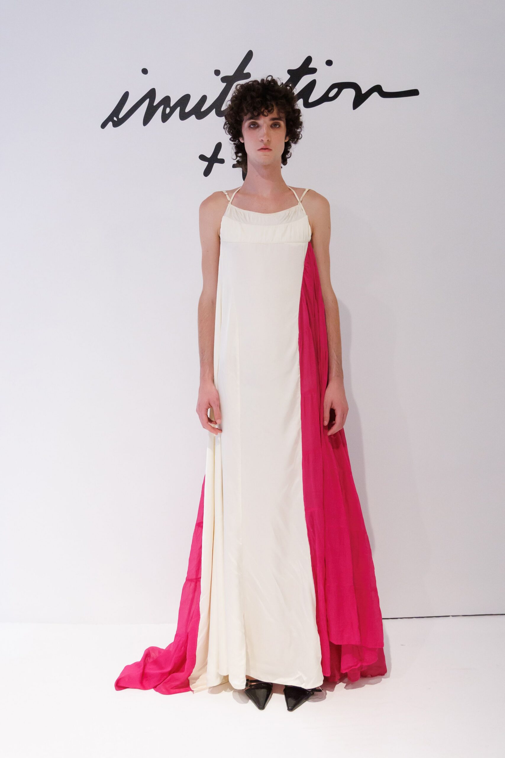 Ivory floor-length slip dress with a softly gathered square neckline. Fuchsia chiffon panel falling from one side into a long trailing sweep. Black patent pointed pumps peeking from the hem. For crossing a hotel ballroom after midnight with the tablecloth still in hand.