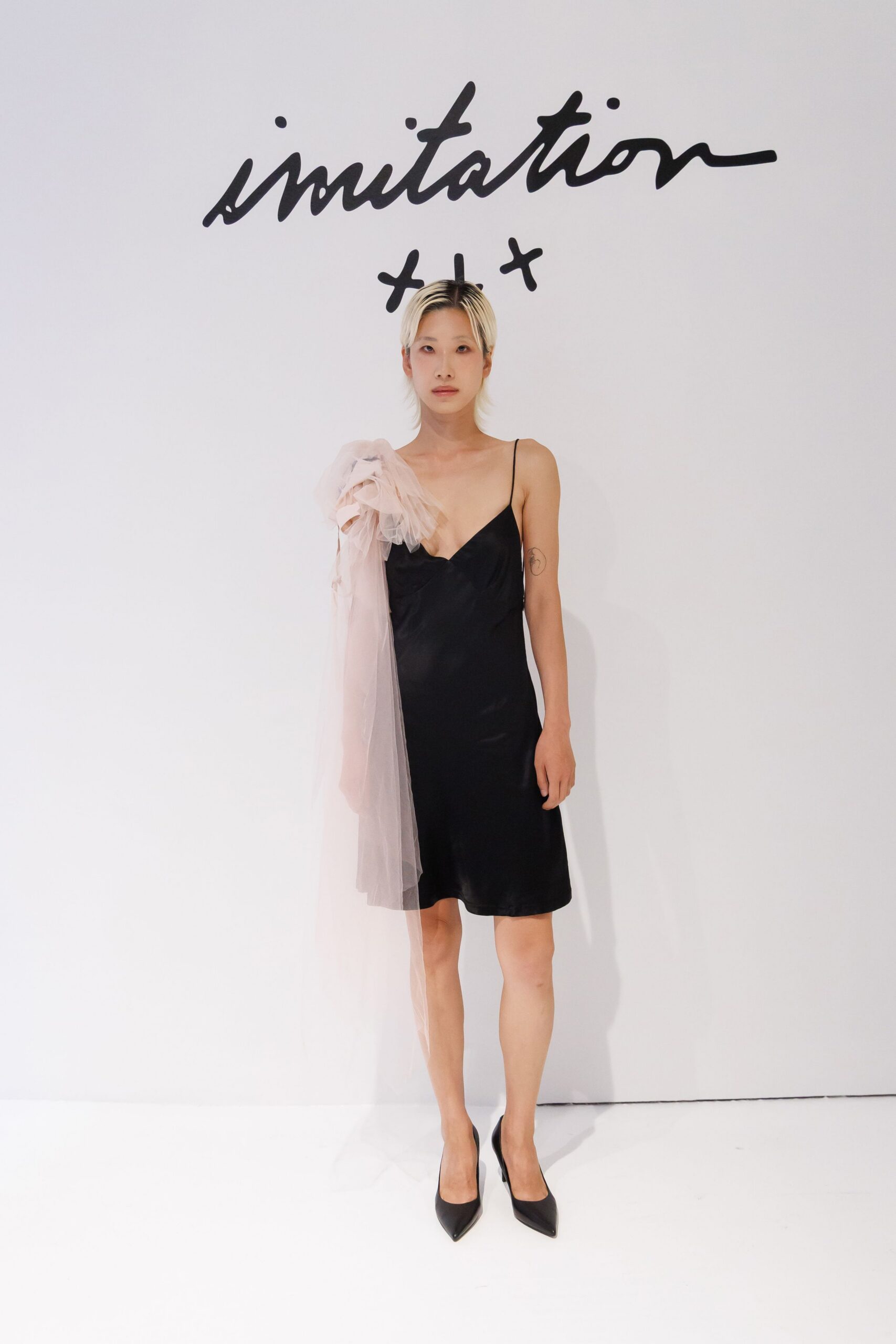 Black satin slip dress, cut on the bias with a dipped neckline. Blush tulle ruffled at one shoulder, falling in a sheer panel. Black pointed pumps. For the wedding afterparty when one corsage survived the night.