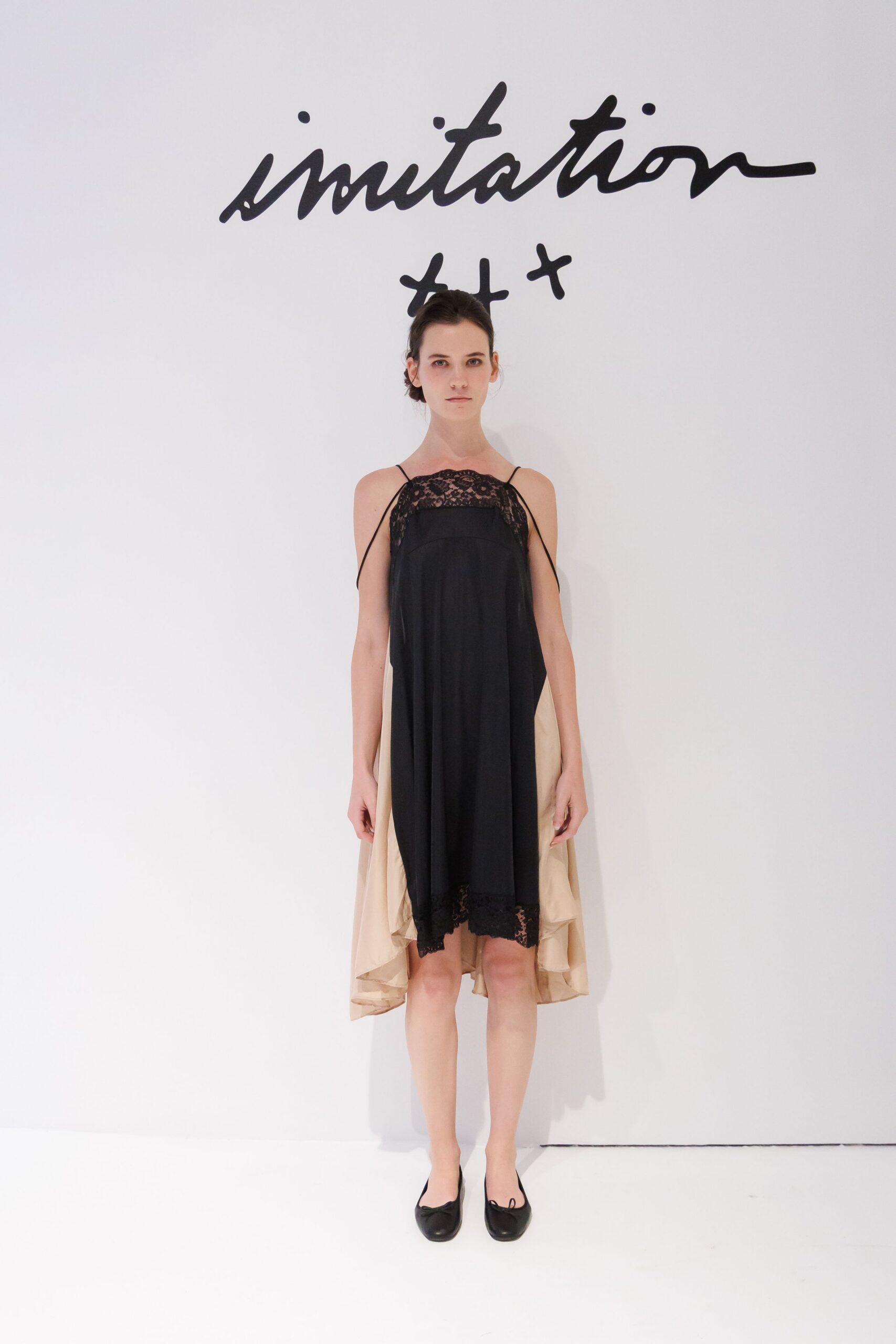 Black slip dress with scalloped lace yoke and loose beige underlayer falling longer behind. Black ballet flats with tiny bow knots at the vamp. After the wedding dinner, carrying your shoes through the hotel corridor.