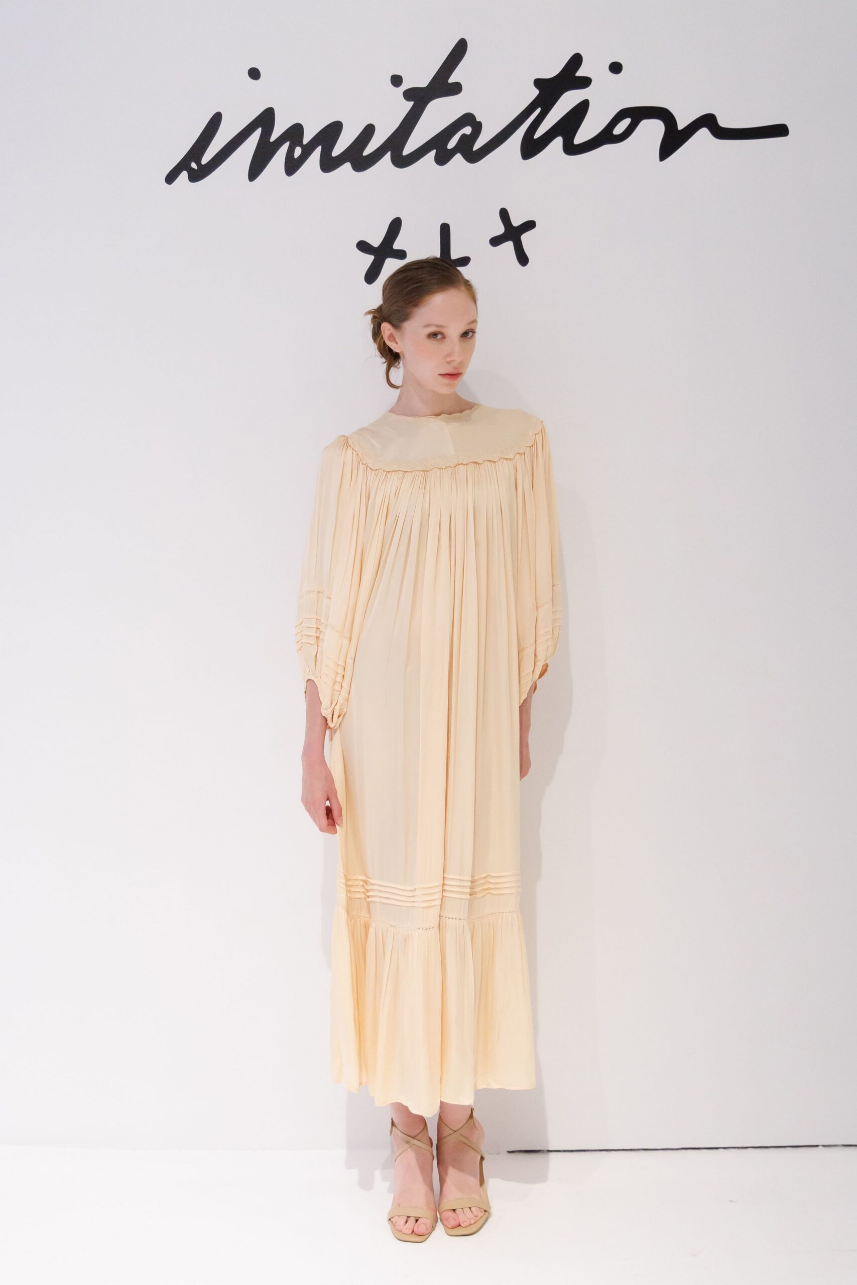 Buttercream voile dress with a broad yoke, fine gathers and pintucked sleeve bands. Nude ankle-wrap sandals with slim crisscross straps. Sunday christening lunch, cake crumbs caught in the tablecloth lace.