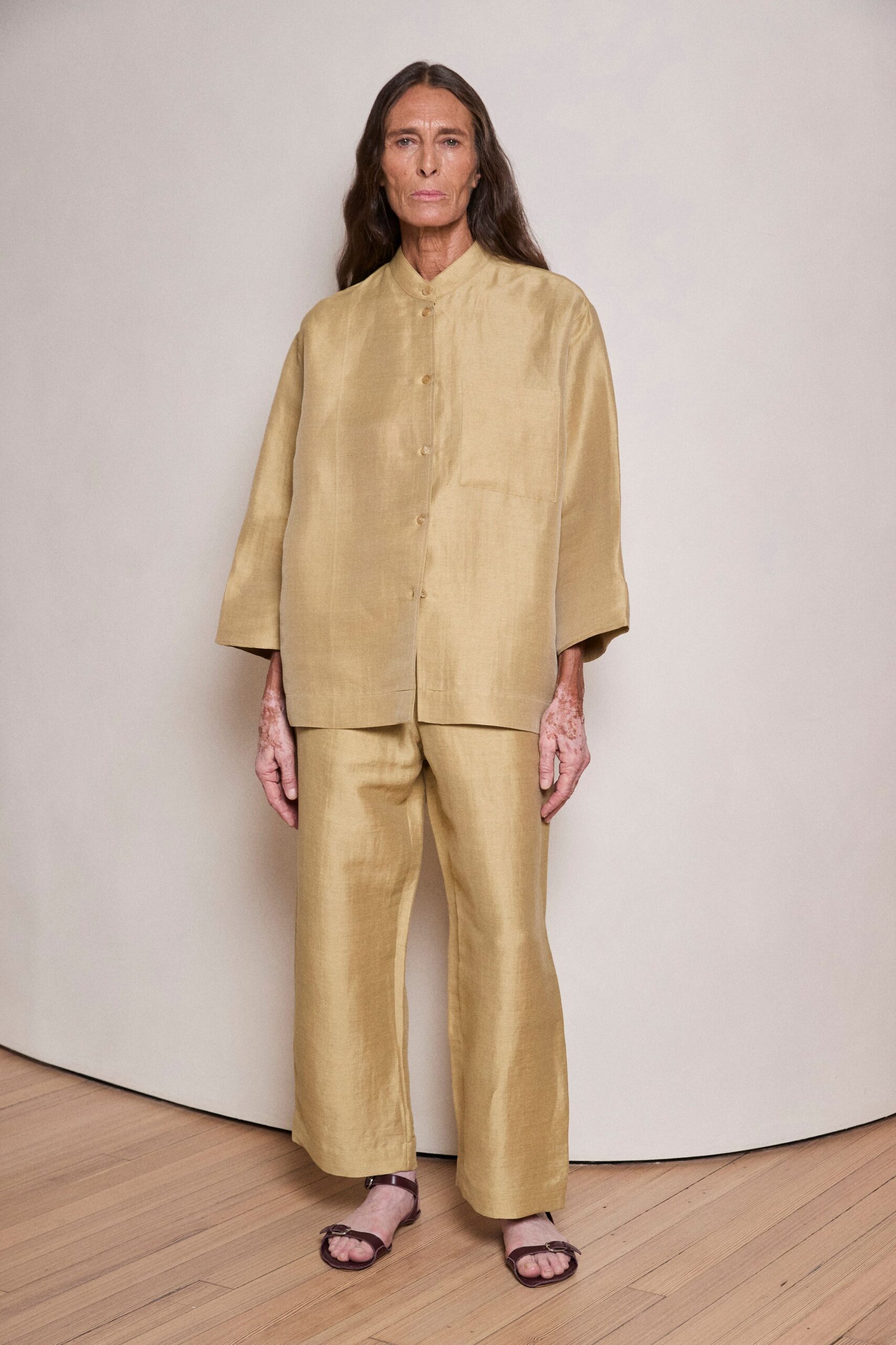 Oat-gold slubbed silk tunic shirt with a neat stand collar. Matching straight trousers, cropped just above the ankle bone. Brown leather sandals with a small side buckle. For buying apricots early, before the pavement starts to radiate heat.