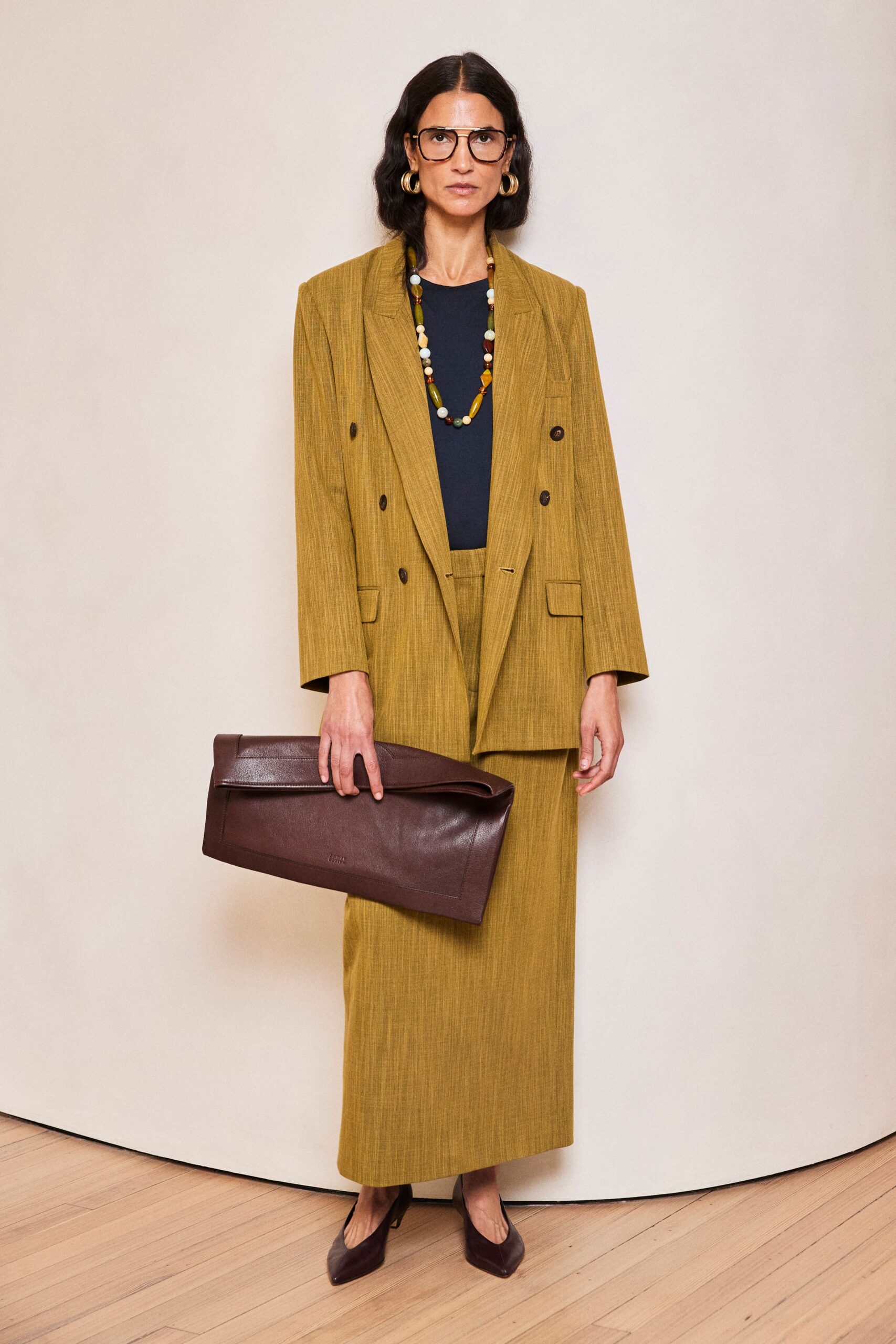 Oversized brown aviator frames. Ochre slub-weave blazer, double-breasted with dark horn buttons. Inky crewneck shell underneath. Matching column skirt, waistband just peeking below the jacket. Oversized espresso leather foldover clutch. Burgundy pointed pumps. For arriving early to a museum board lunch with papers still in hand.