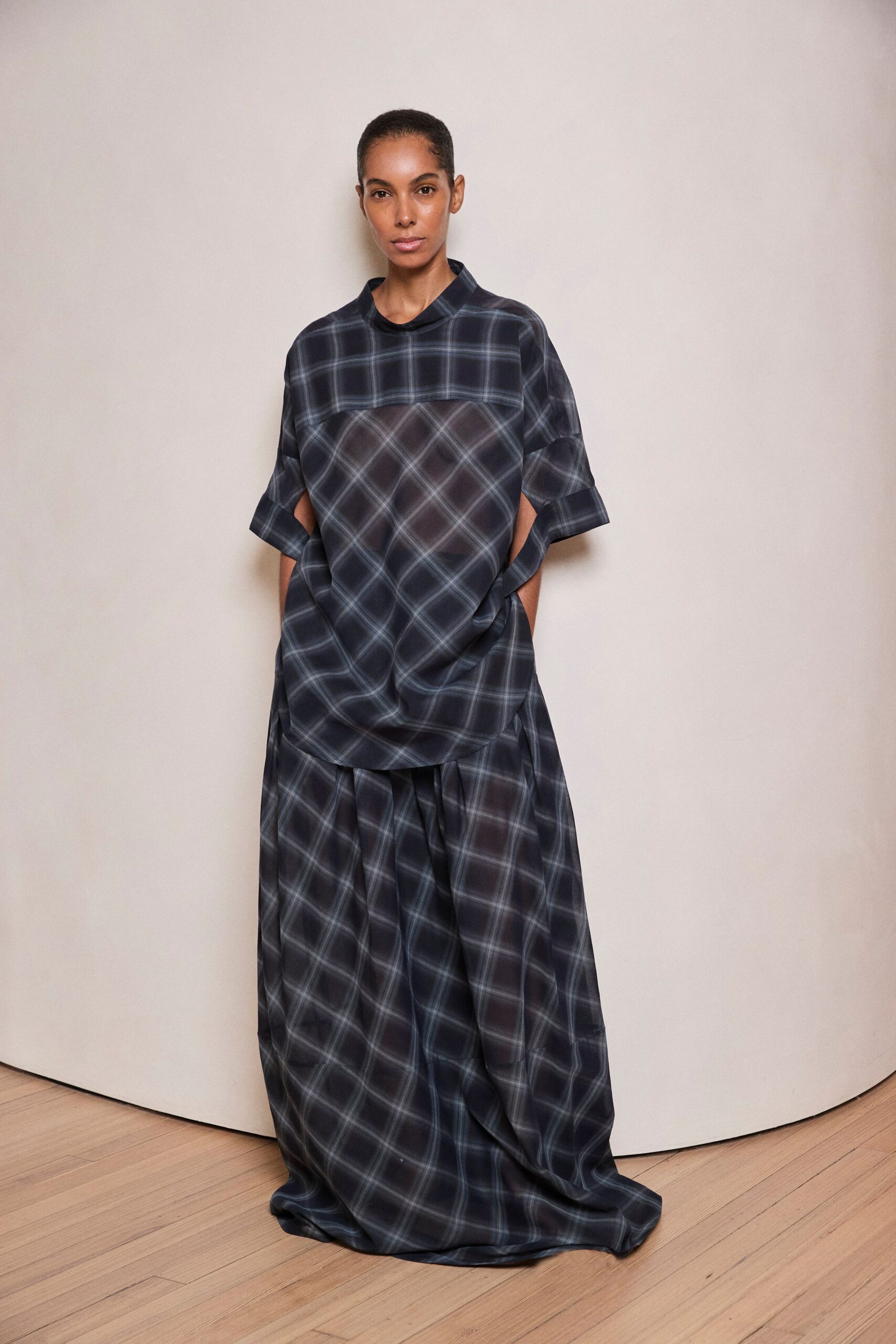 Smoke plaid tunic with a yoke cut crosswise and deep side openings. Matching floor-length skirt, gathered full with broad inverted pleats. Walking the long corridor after everyone else has gone upstairs.