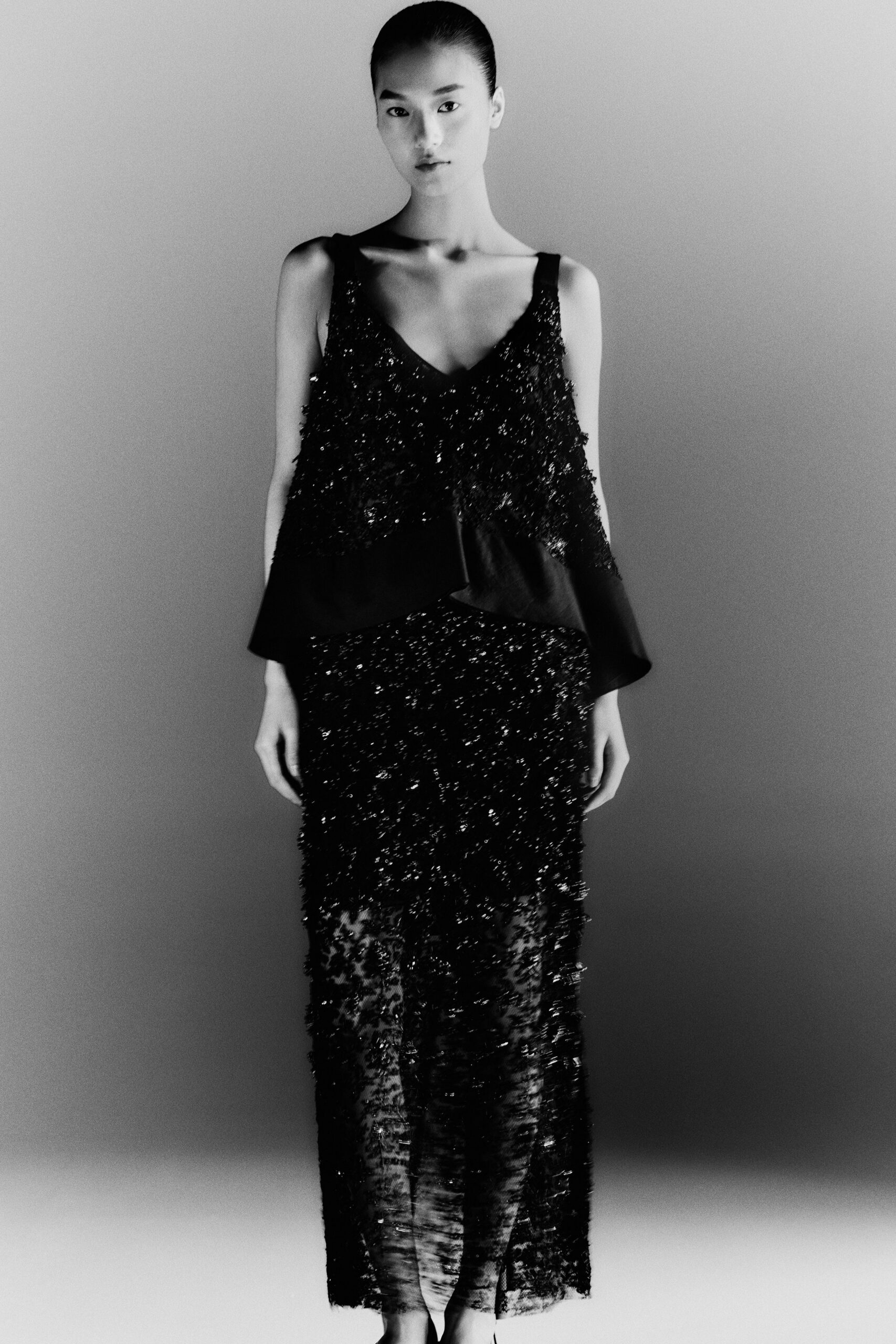 Black spaghetti-strap top in shaggy sequined lace, cut away at one shoulder. Matching ankle-length skirt, sheer at the hem with dense glittering fringe. Whatever you wear to stand by the hotel window after midnight rain.