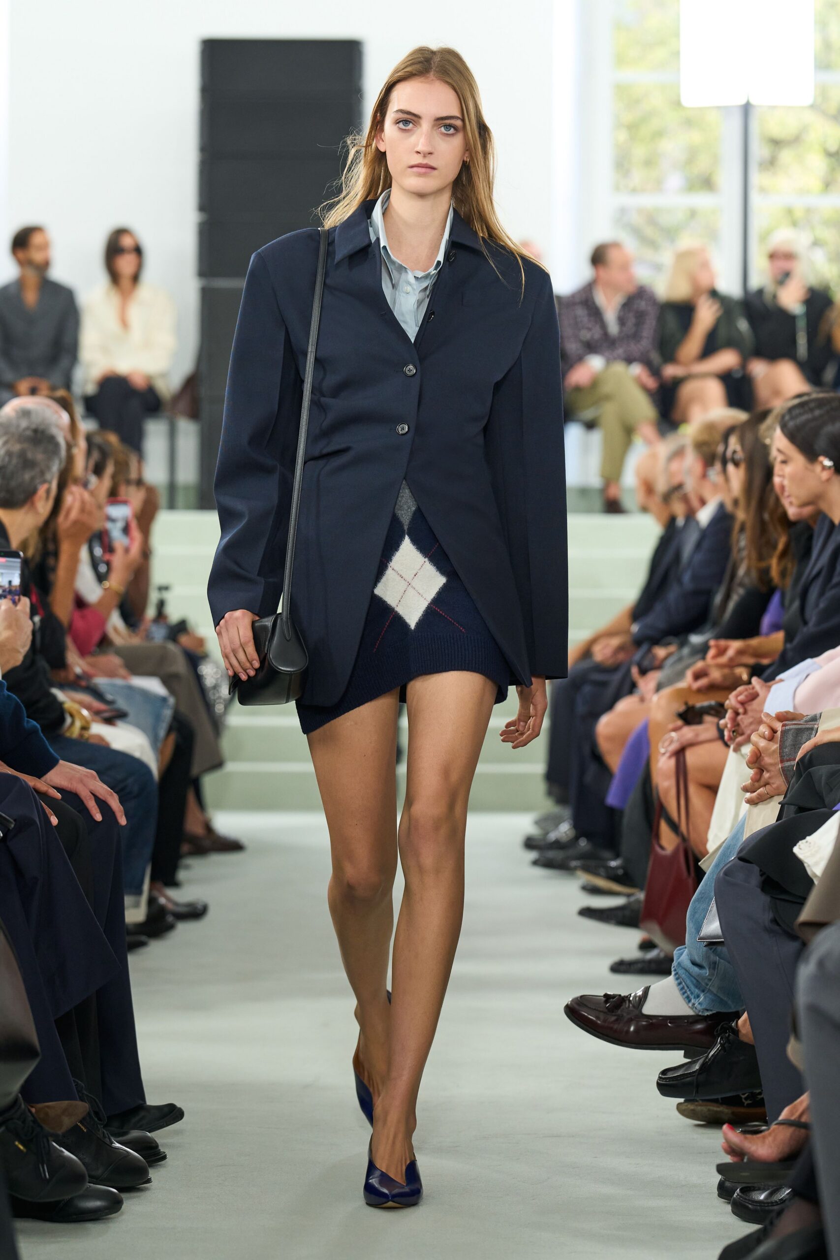 Long navy blazer nipped through the waist with two dark buttons. Pale blue shirt, collar slightly rumpled under the lapels. Navy knit mini with a large white argyle diamond. Small black leather bag on a narrow shoulder strap. Indigo pumps with squared vamps. For crossing the quad after office hours with borrowed library books.