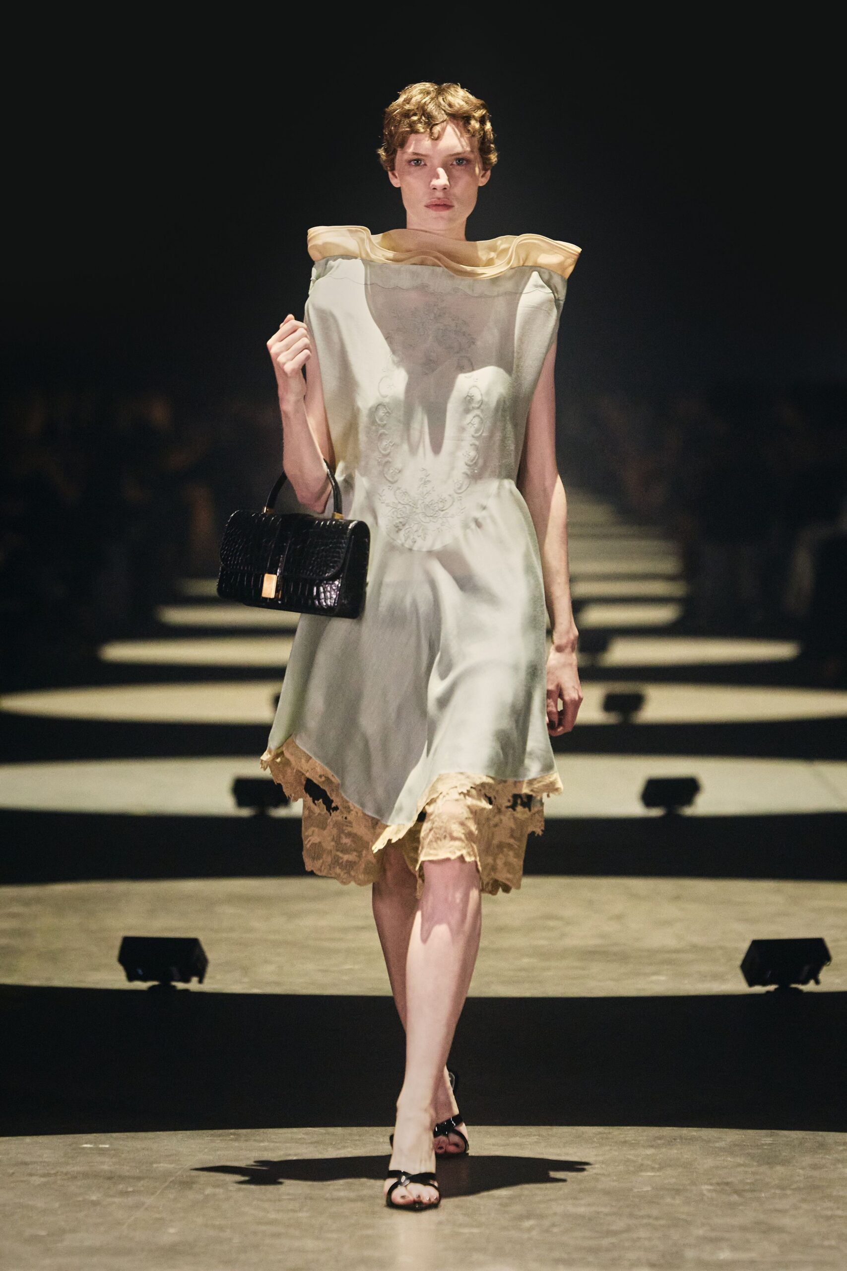 Sheer ivory slipdress with a rolled champagne organza collar. Tea-stained lace underlayer hanging below the uneven hem. Black crocodile-embossed top-handle bag with a gold clasp. Black patent thong sandals. For reading the hotel guestbook after everyone else has gone upstairs.