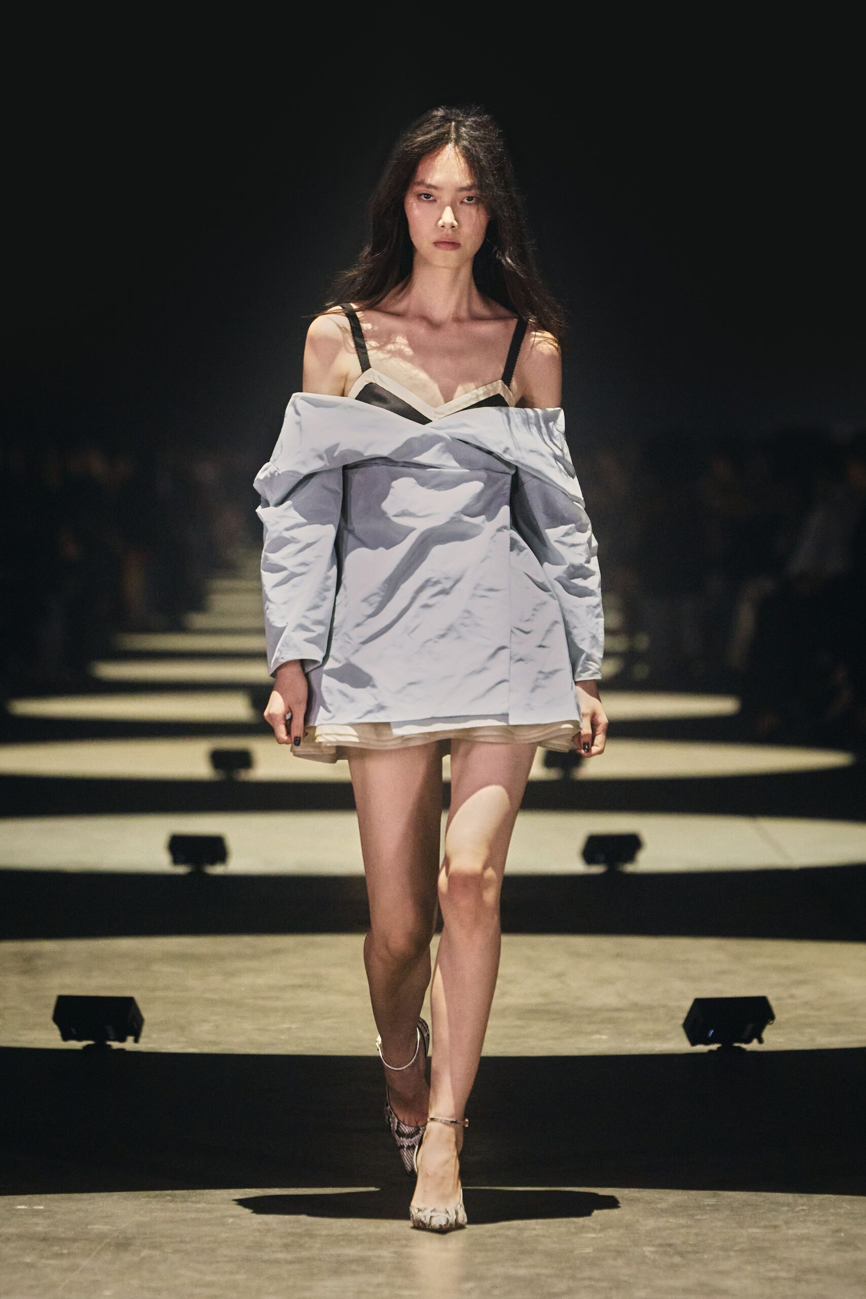 Powder-blue taffeta mini dress, shirting folded off the shoulders in crisp creases. Ivory slip peeking below, scalloped neckline held by black straps. Pointed pumps in pale python print with thin ankle straps. For the walk home after a wedding where you took off the jacket hours ago.