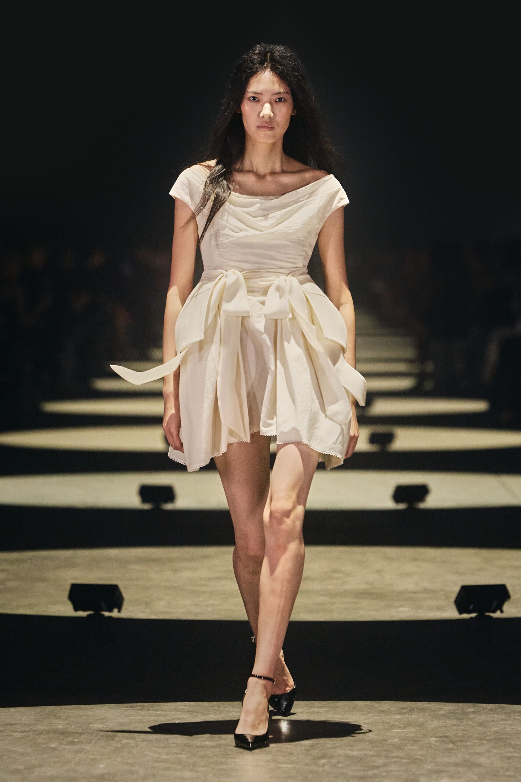 Ivory mini dress with a folded bateau neckline and oversized waist bows. Black patent pumps with a sharp pointed toe. City hall wedding, then straight to the noodle shop still holding the flowers.