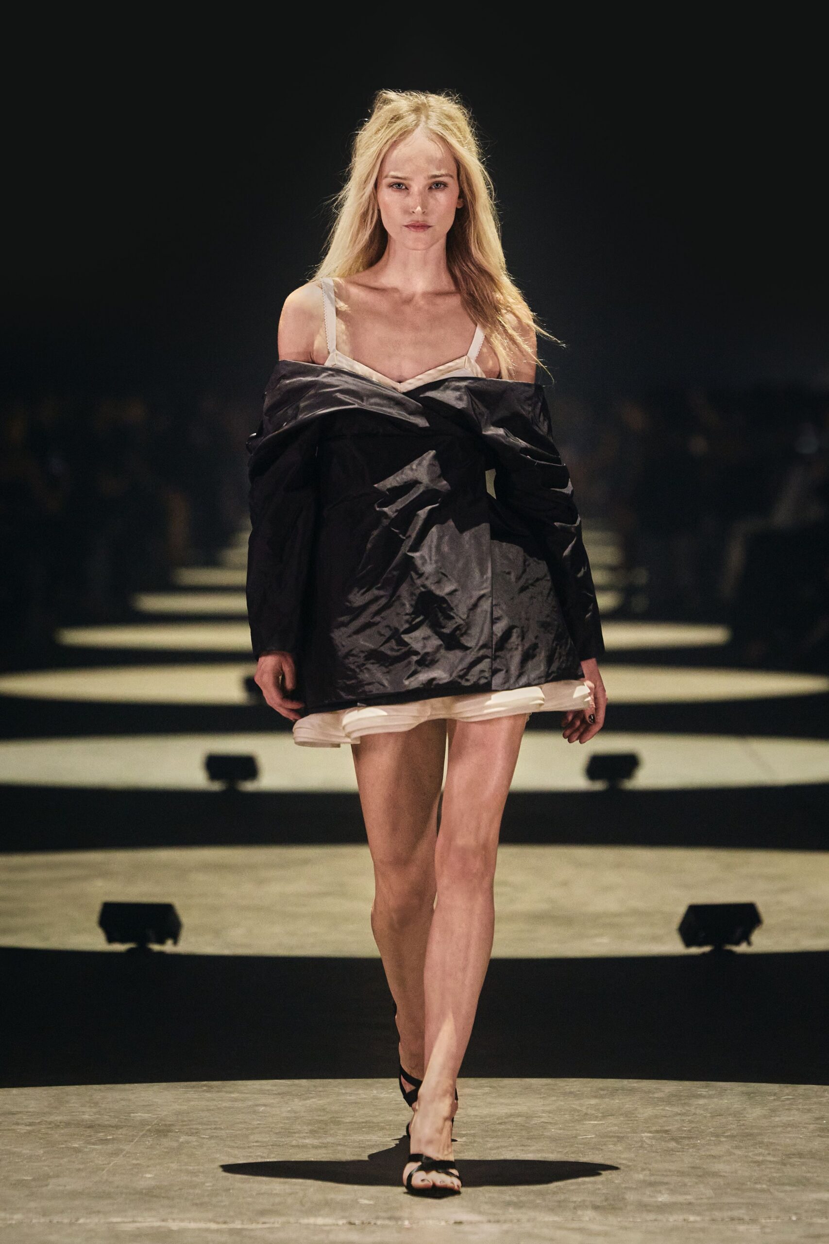 Ivory slip dress with narrow straps and a doubled chiffon hem. Black crinkled coat shrugged off the shoulders, one fold biting across the bust. Black toe-loop sandals. Whatever you throw on for dawn room service after sleeping in yesterday's makeup.