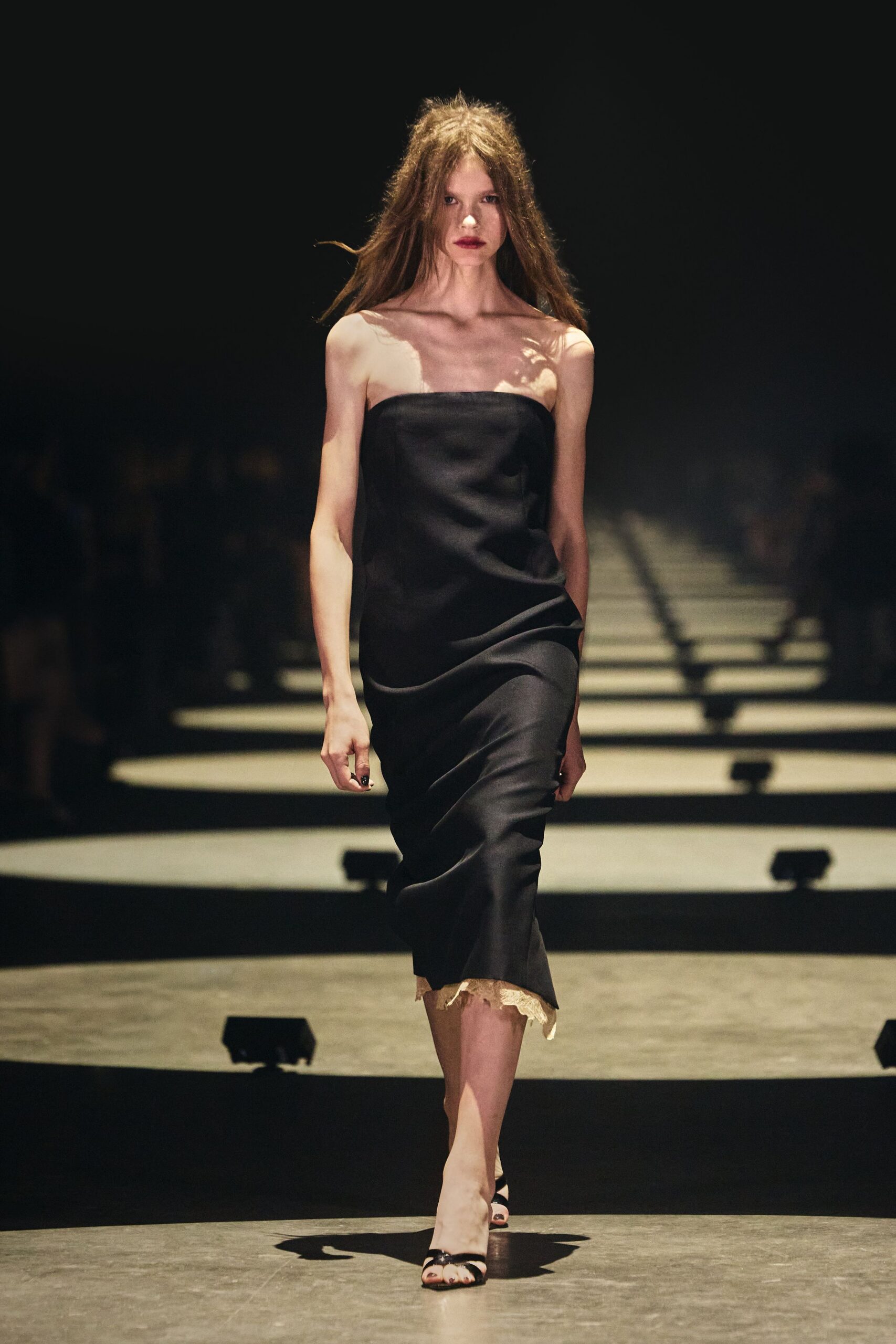 Black strapless satin slip dress, ivory lace peeking from the uneven hem. Black patent thong sandals, narrow straps glossing the toes. Whatever you pull on for a hotel bar after midnight room service.