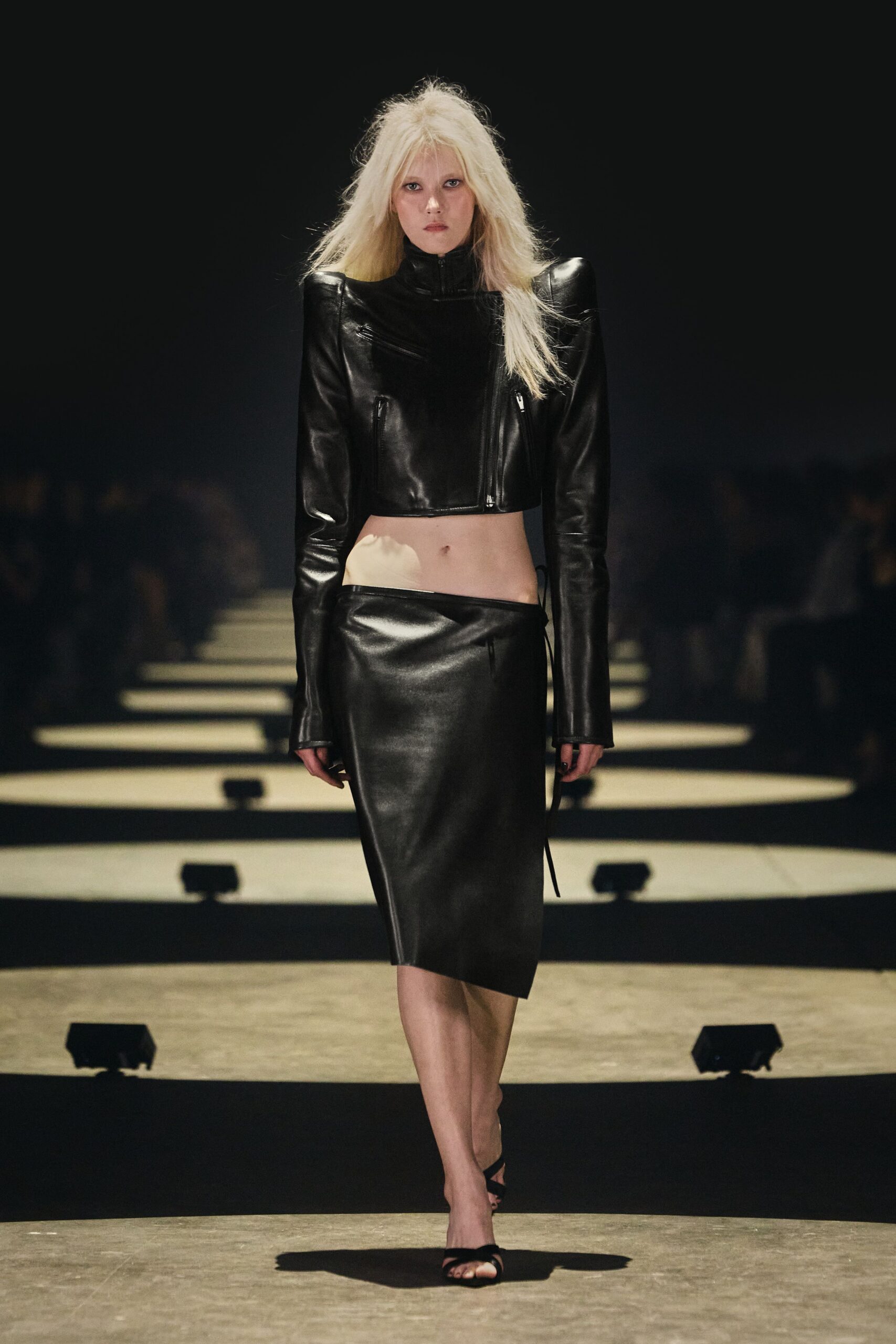 Cropped black leather jacket with squared shoulders and skewed zip pockets. Low-slung black leather pencil skirt, one tie end hanging at the hip. Barely there black heeled sandals. Whatever you wear to miss the last train and keep walking.