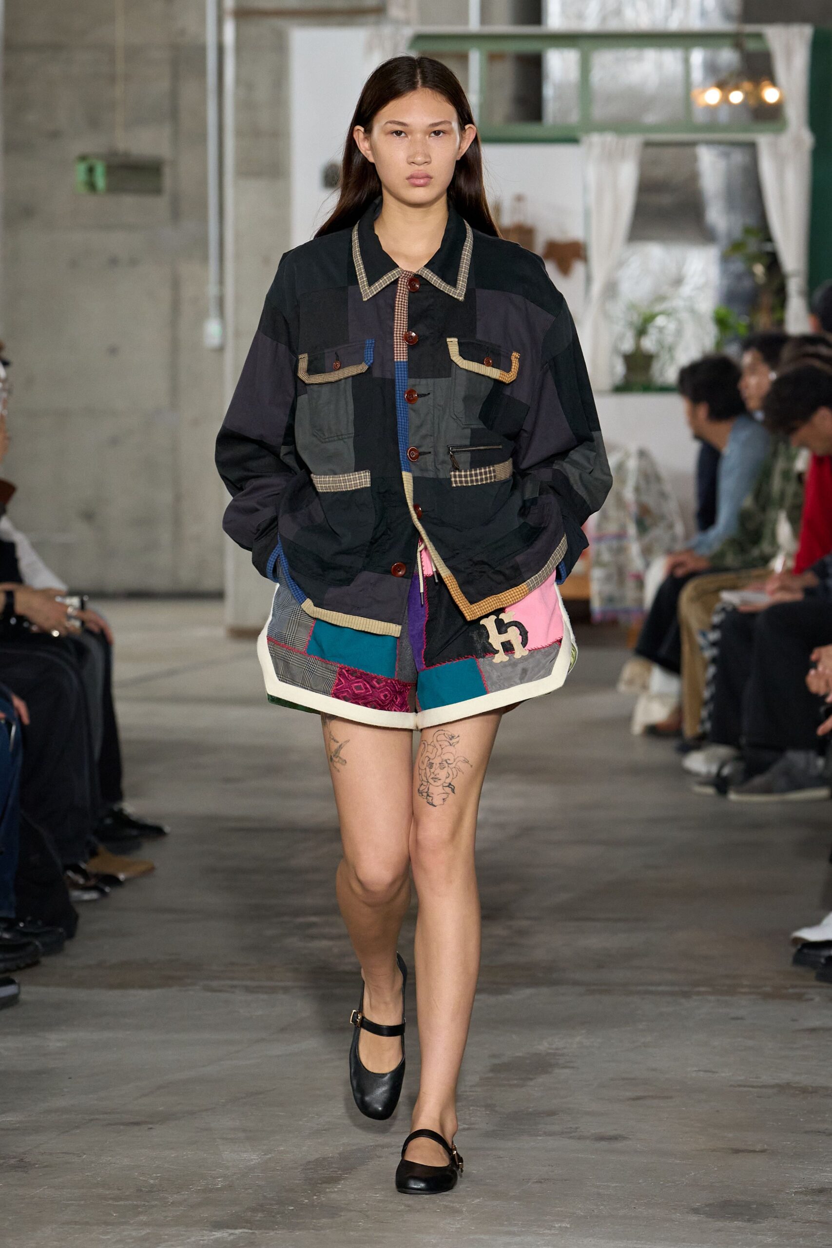 Oversized patchwork jacket in washed black panels, checked binding and tortoiseshell buttons. Quilted patchwork shorts with glen plaid, teal blocks and a cream appliqued H. Black Mary Jane flats with slim buckle straps. Walking back from the corner store in borrowed clothes and house slippers.