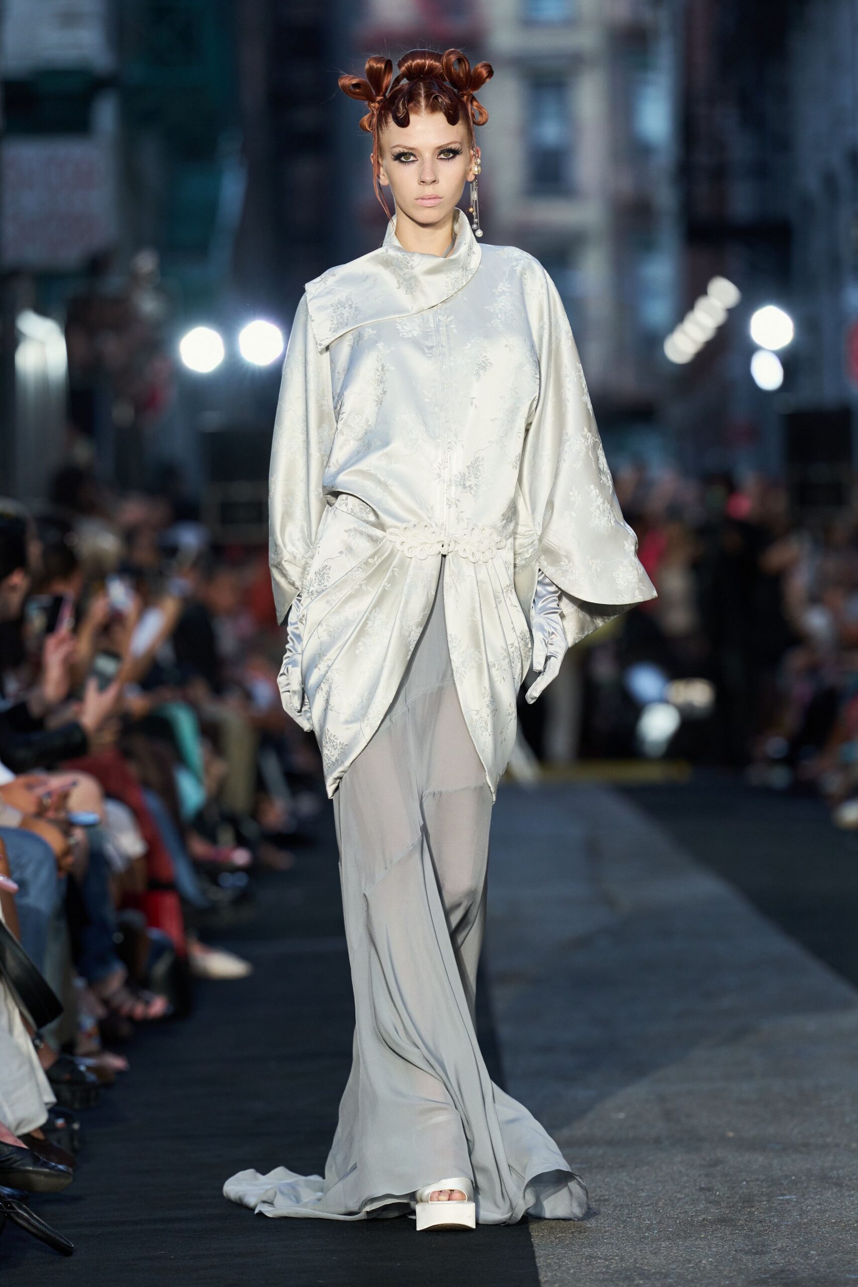 Pearl brocade tunic with a folded asymmetric collar and looped waist trim. Matching satin gloves, softly ruched at the wrists. Misty grey trousers in liquid jersey, pooling into a small train. White satin platforms, square at the toe. For drifting through a hotel corridor after someone else's winter wedding.