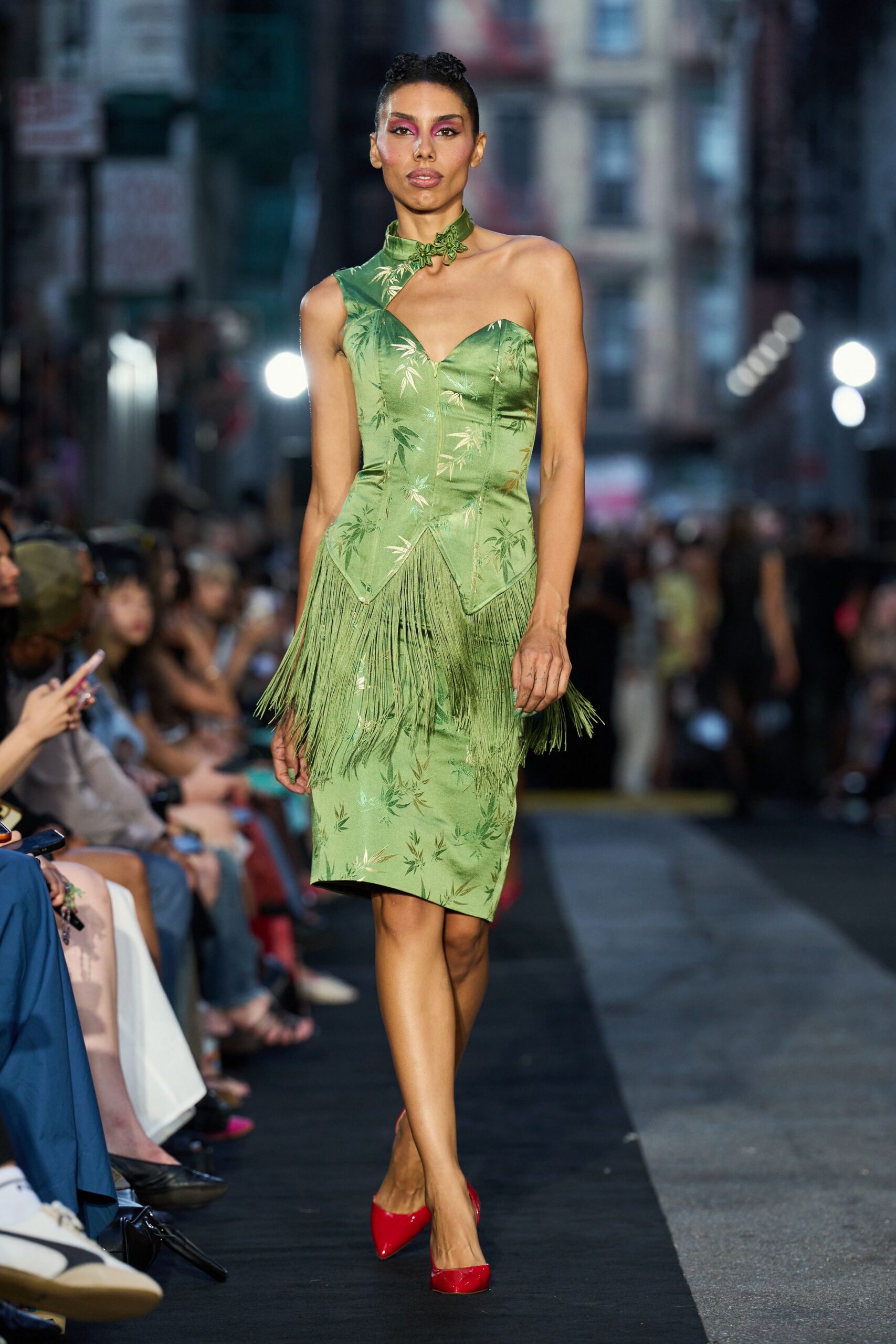 Celadon satin dress with bamboo jacquard, one-shoulder bodice and long fringe. Matching satin choker fastened with a frog-knot flourish. Red patent pumps. Crossing Chinatown at dusk after dinner, orchids wrapped in butcher paper.