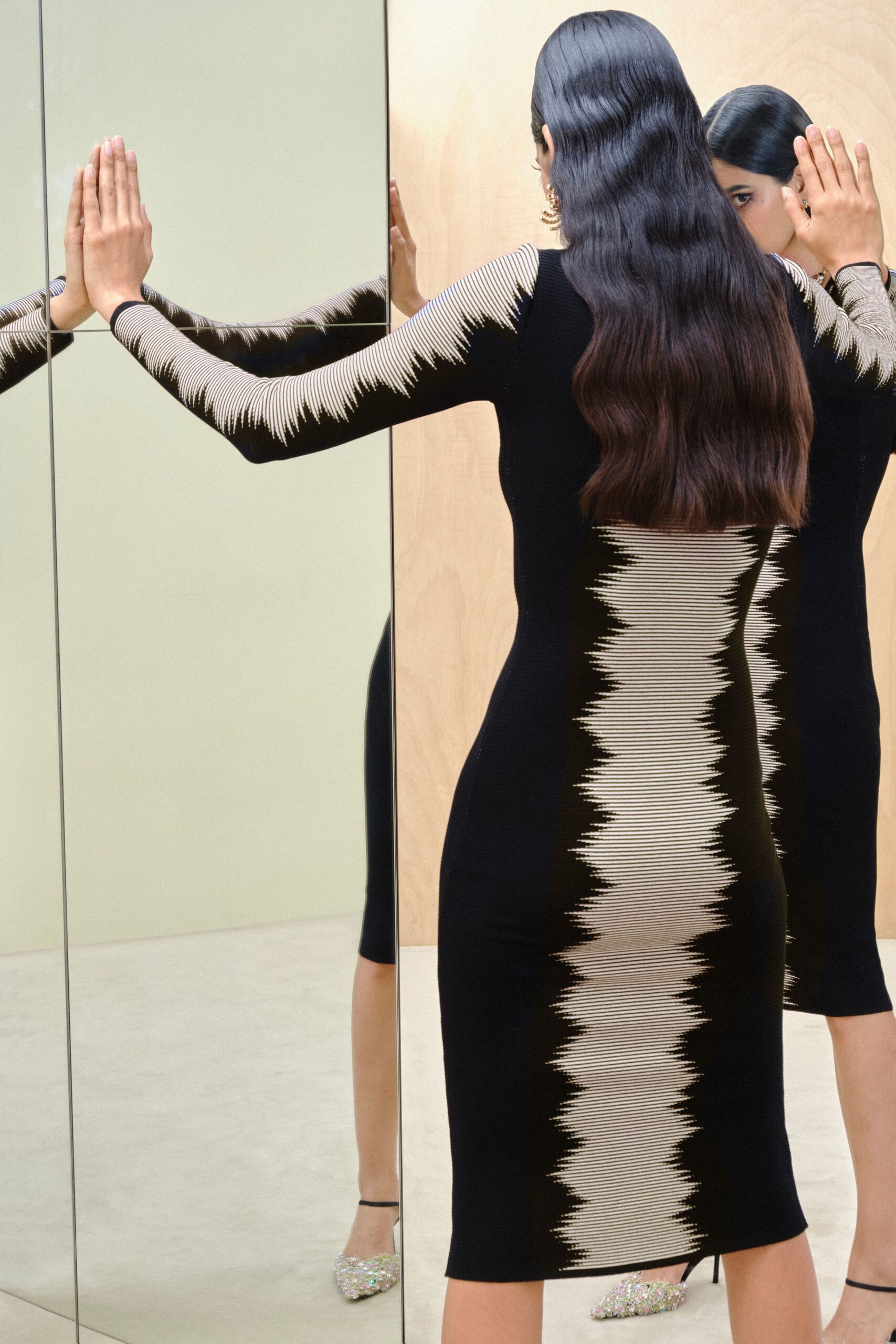 Black ribbed knit midi dress, ivory zigzag stripes running down sleeves and spine. Crystal-encrusted slingback pumps catching hard light at the pointed toe. Tiered gold hoops at one ear. Checking yourself in a mirrored hallway before the penthouse door opens.
