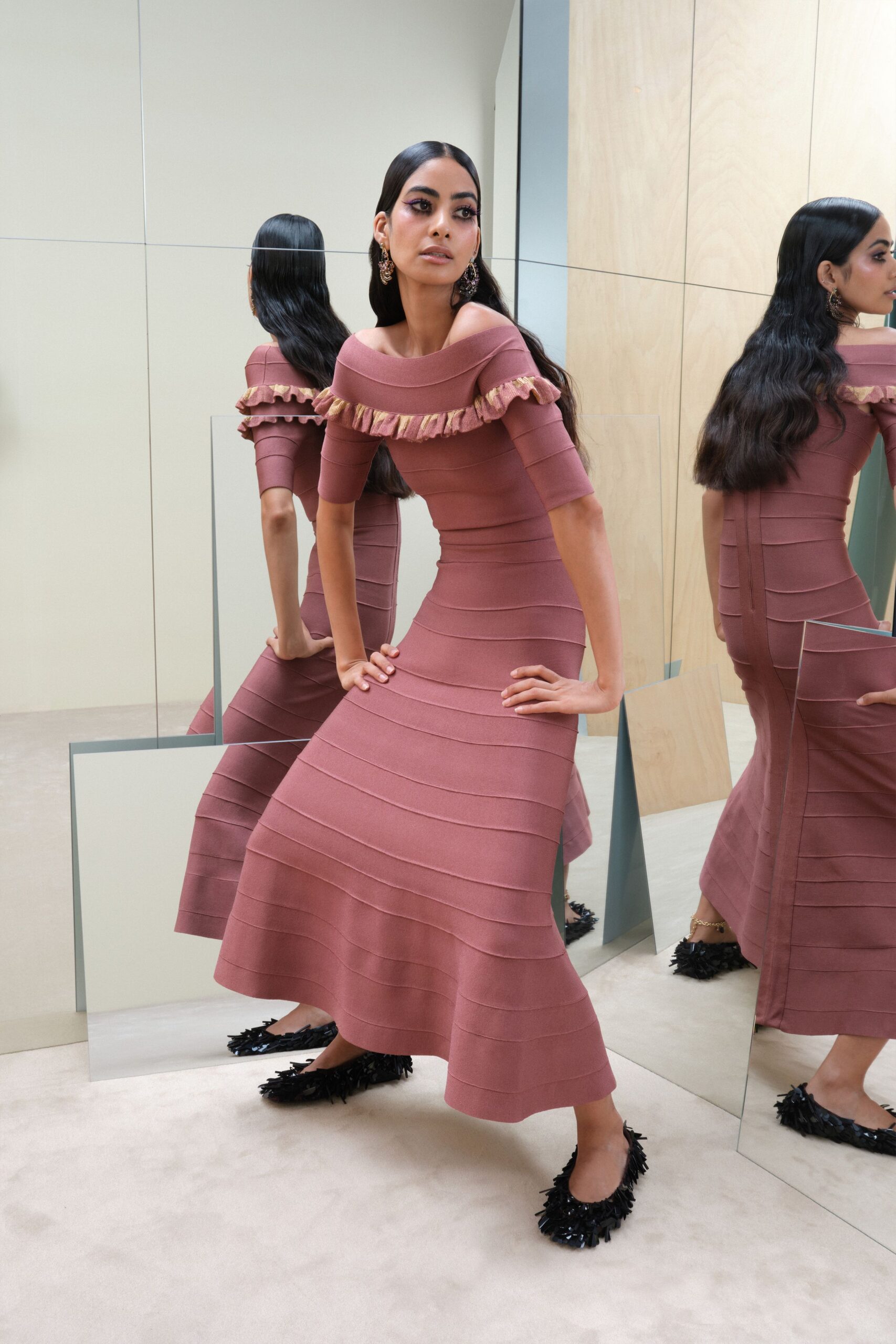 Dusty rose bandage-knit dress with a folded off-shoulder neckline and metallic ruffle. Dangling filigree clusters brushing the jaw. Black pointed flats buried under shaggy paillettes. Trying on the good dress while every mirror in the apartment disagrees.