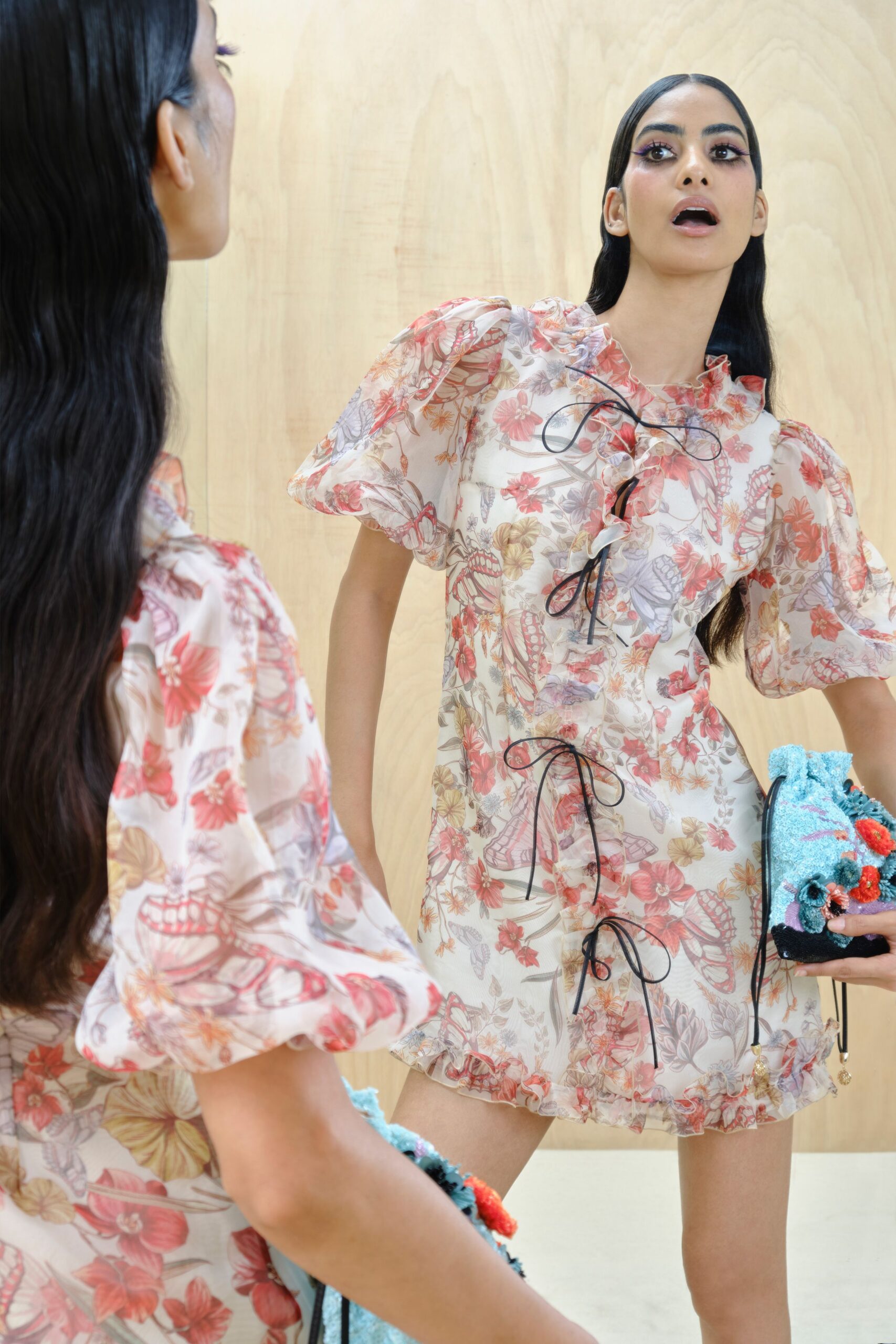 Sheer organza minidress printed with coral flowers and pale butterflies, black ribbon bows down the ruffled front. Fuzzy aqua pouch crowded with tufted flowers and a dangling charm. Trying on too much perfume in a hotel boutique by the sea.