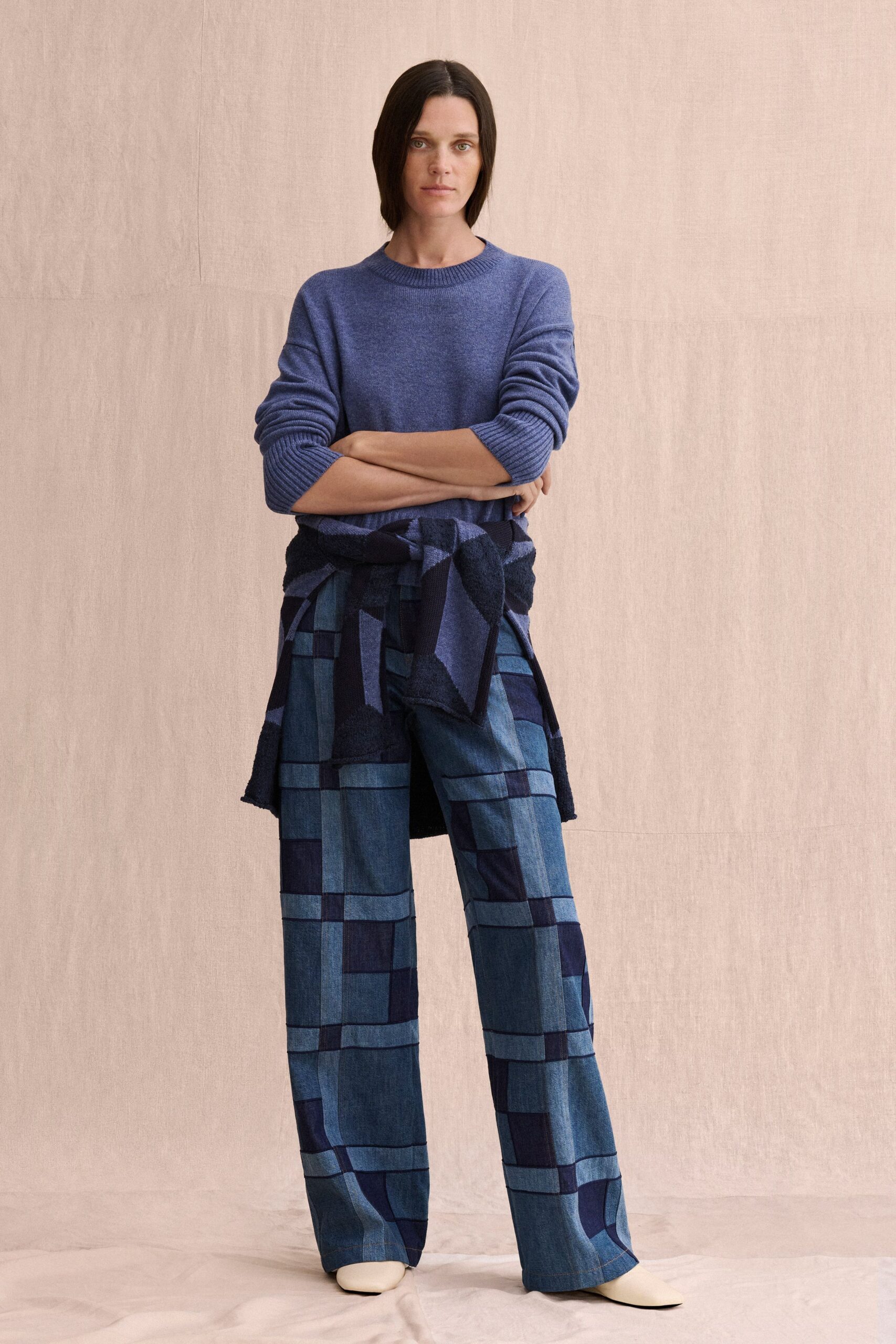 Heathered cornflower crewneck knit, sleeves pushed into thick ribbed stacks. Geometric navy and indigo knit tied low around the hips. Wide-leg patchwork denim trousers, grid pieced in washed and dark blues. Cream leather square-toe boots peeking under the hem. For a Sunday museum shift before the front doors open.