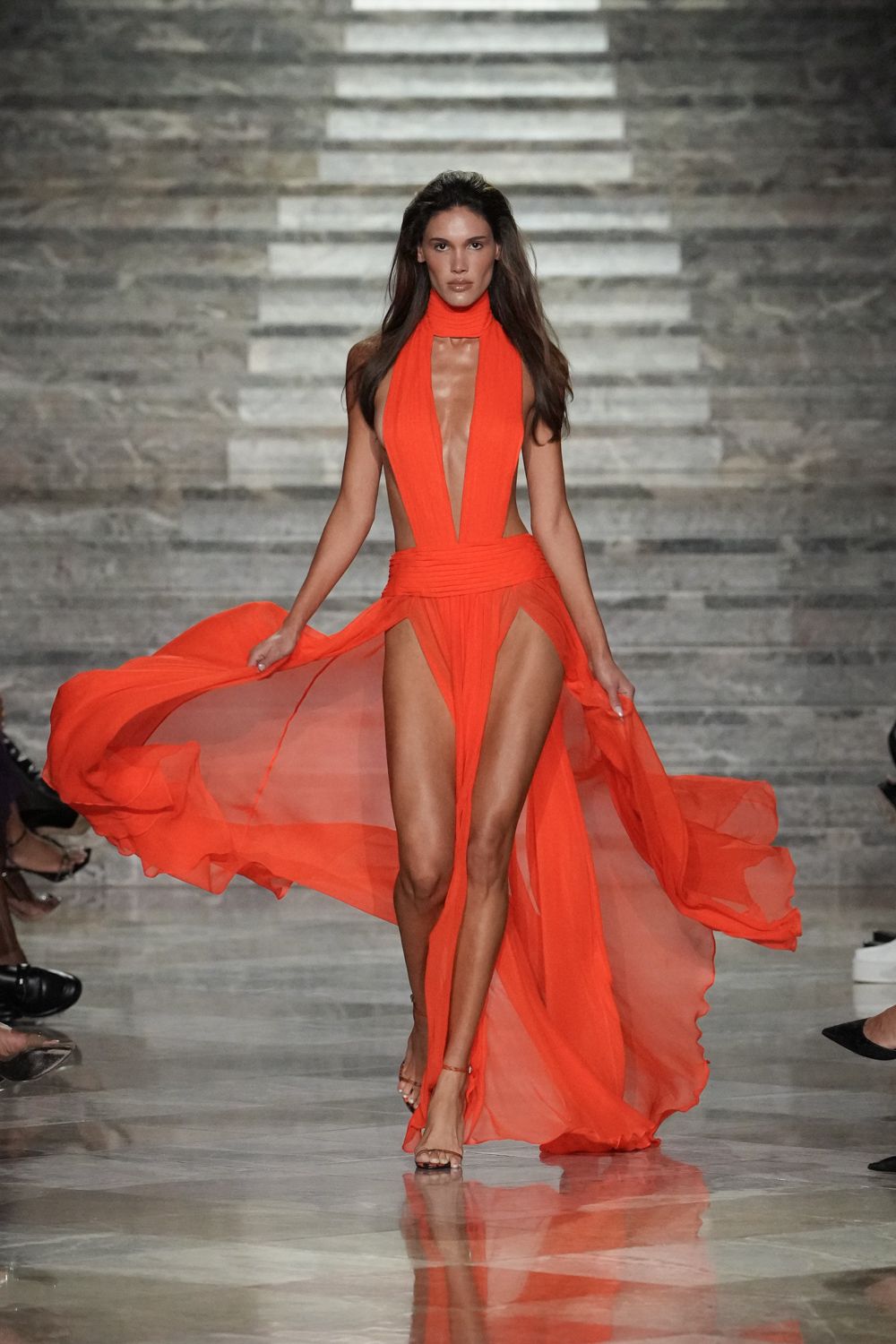 Scarlet chiffon halter gown with a plunging cutout and gauzy split overskirt. Barely there ankle-strap sandals, one tiny buckle glinting at the side. For crossing a hotel terrace just as the wind lifts off the sea.