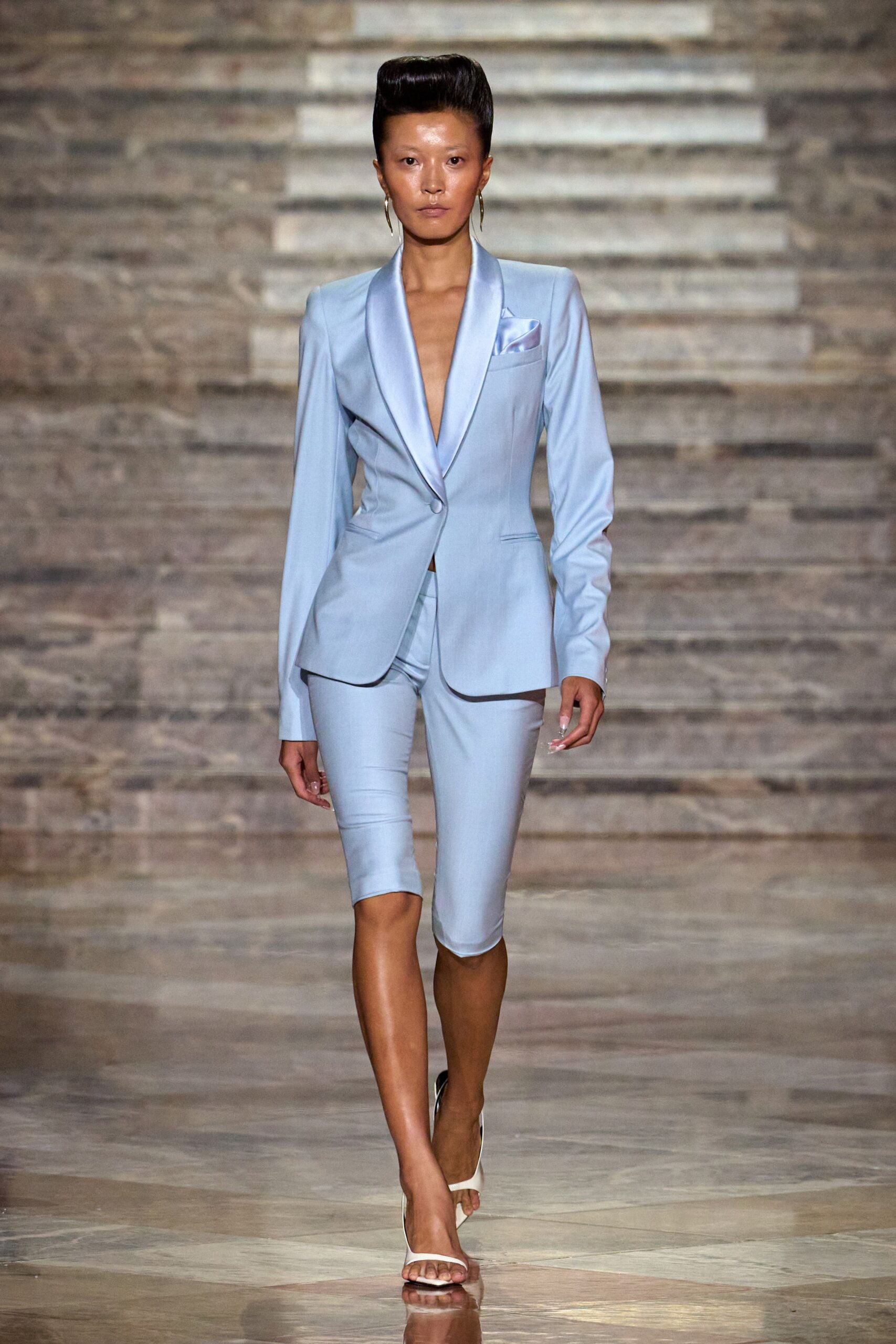 Powder-blue blazer with satin shawl lapels and a lilac pocket square. Matching knee-length shorts, cut close and smooth through the thigh. Thin gold hoops. White thong-strap heels. Courthouse wedding at noon, then champagne on the hotel terrace.