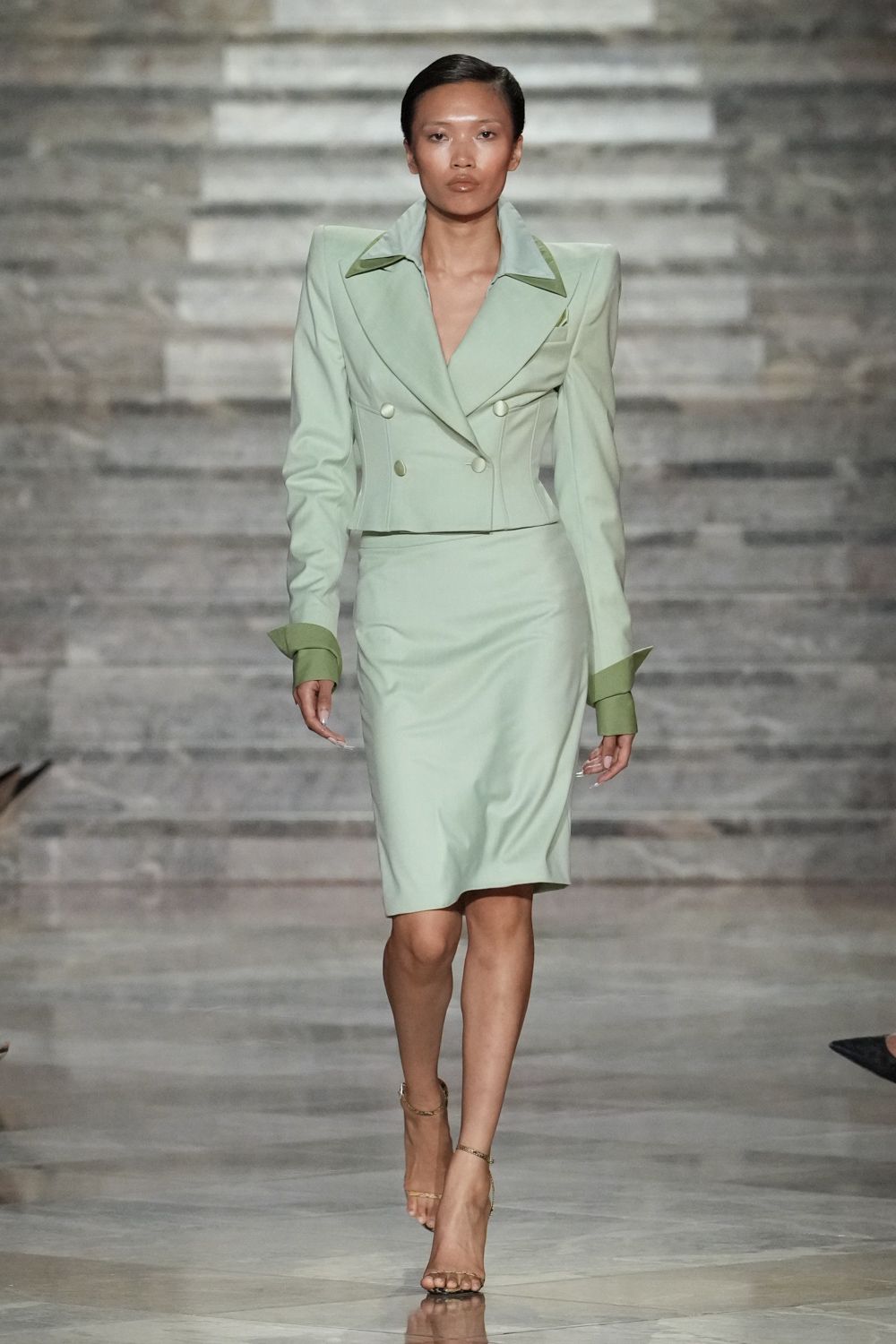 Mint cropped blazer with pagoda shoulders, olive collar tips and turned cuffs. Matching pencil skirt, smooth over the hips with a slight pucker at one knee. Barely there gold ankle-strap sandals. For arriving early to a wedding in a hotel built from pale stone.