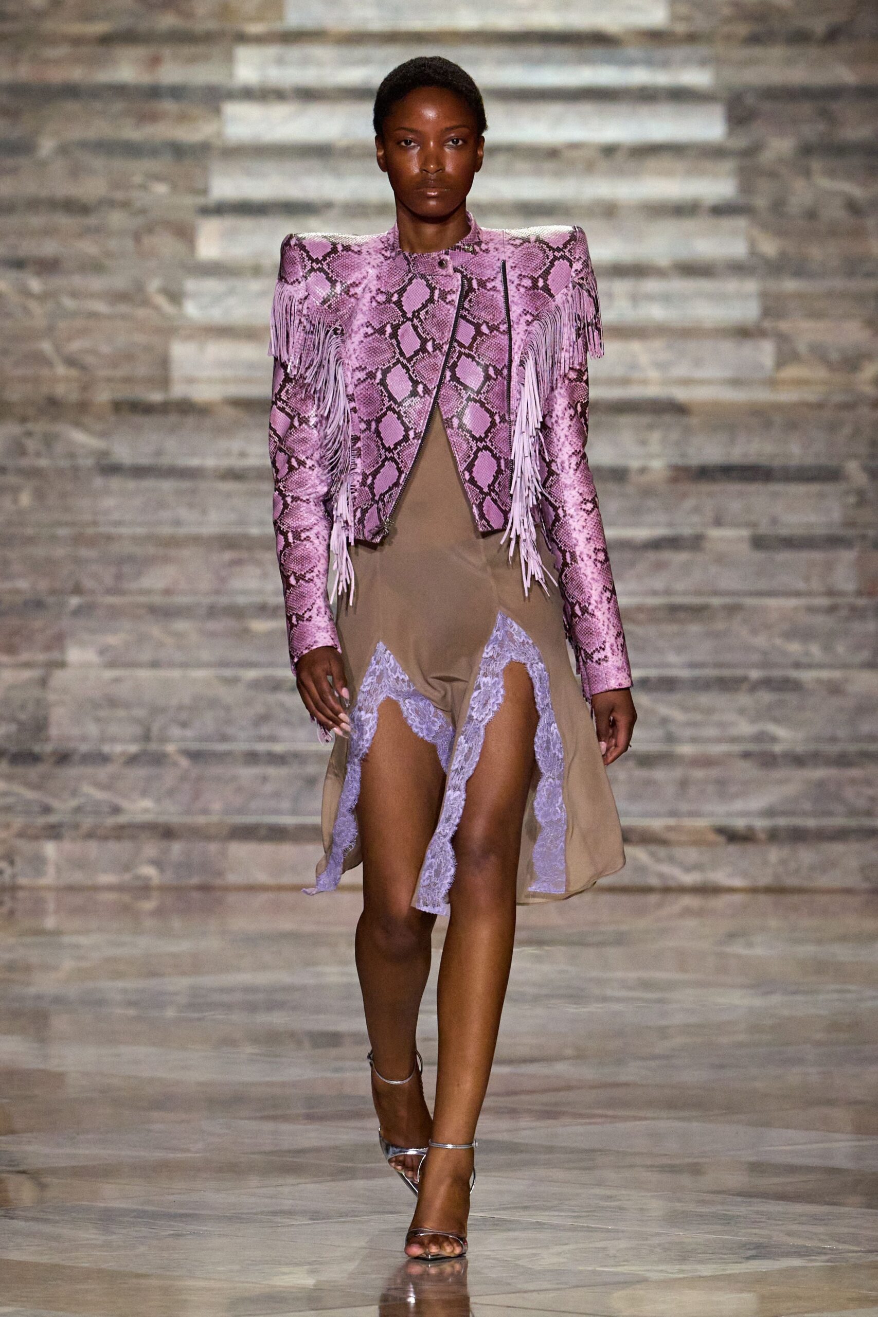 Pink python-print leather jacket with squared shoulders and lilac fringe. Taupe slip dress sliced open with scalloped lilac lace panels. Bare silver ankle-strap sandals. Walking out of a desert wedding after the band has packed up.