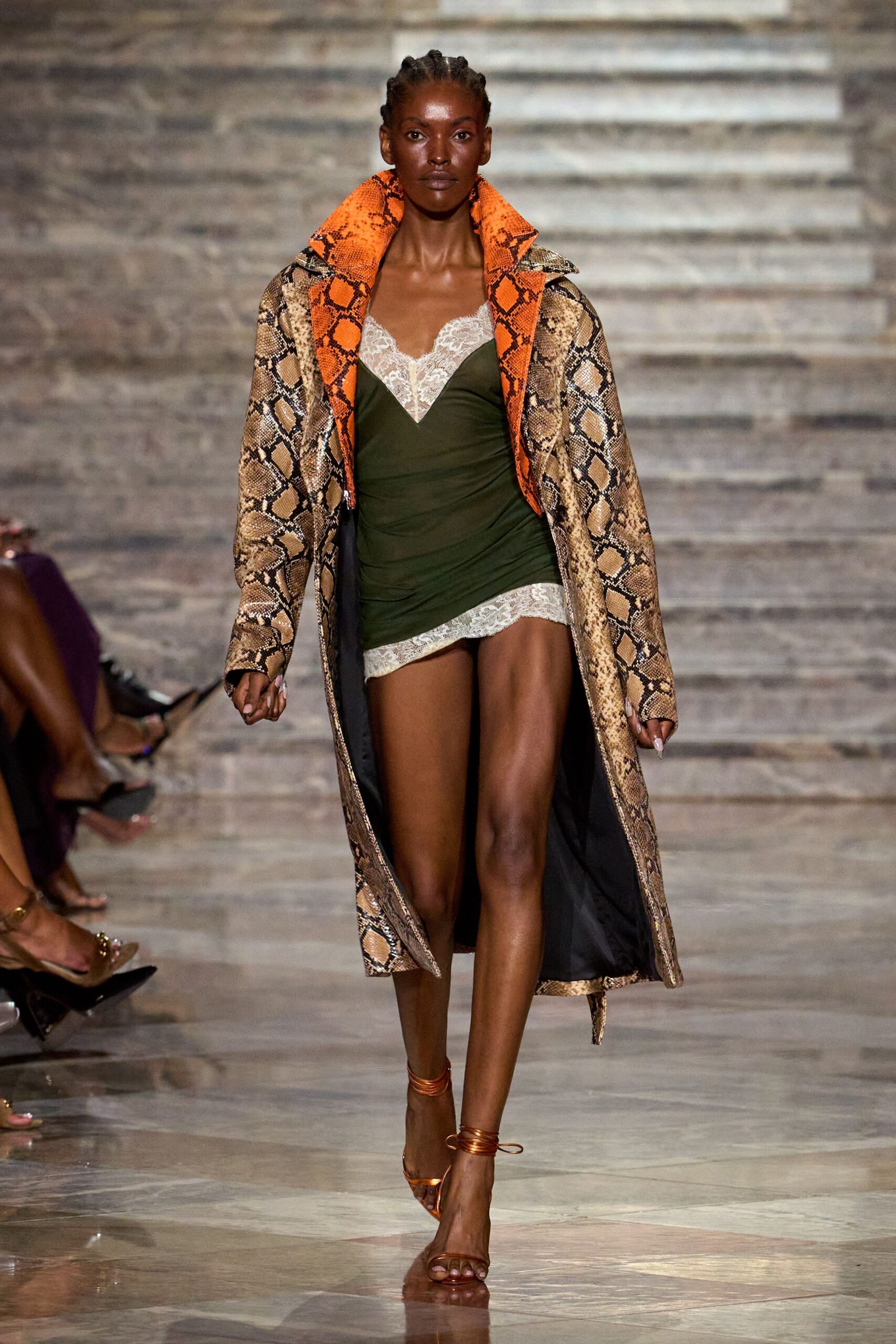 Long python-print coat with a blaze-orange snakeskin collar turned high. Olive jersey slip dress, ruched through the waist with ivory lace edges. Copper wrap sandals, cords coiling twice at the ankle. Walking back from a beach bar after sunset, coat thrown over nightwear.
