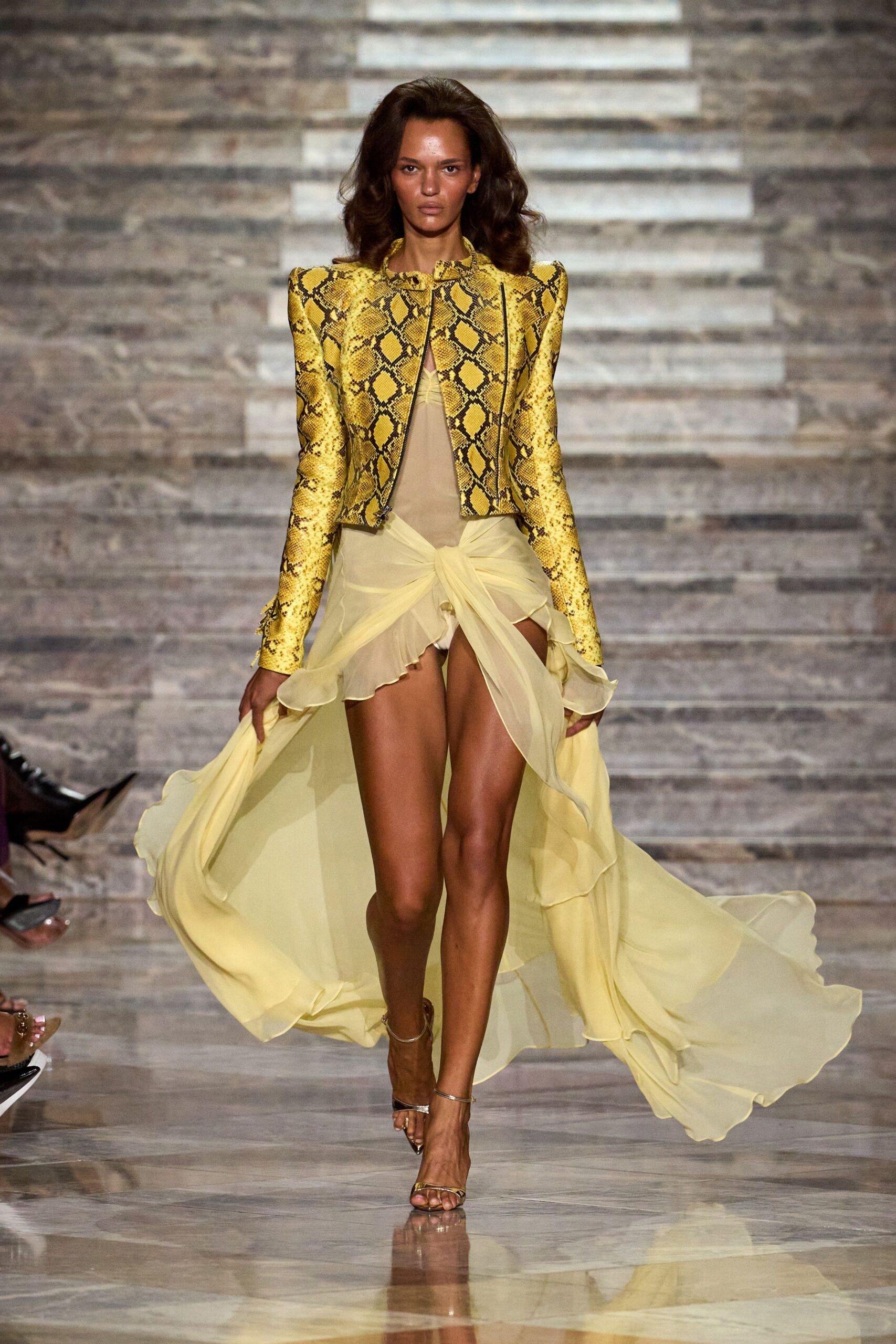Ochre python jacket with razor shoulders and an open metal zip. Butter chiffon slip dress, twisted high slit and long trailing back. Barely-there metallic ankle-strap sandals. Walking out to a hotel terrace just before the storm finally breaks.