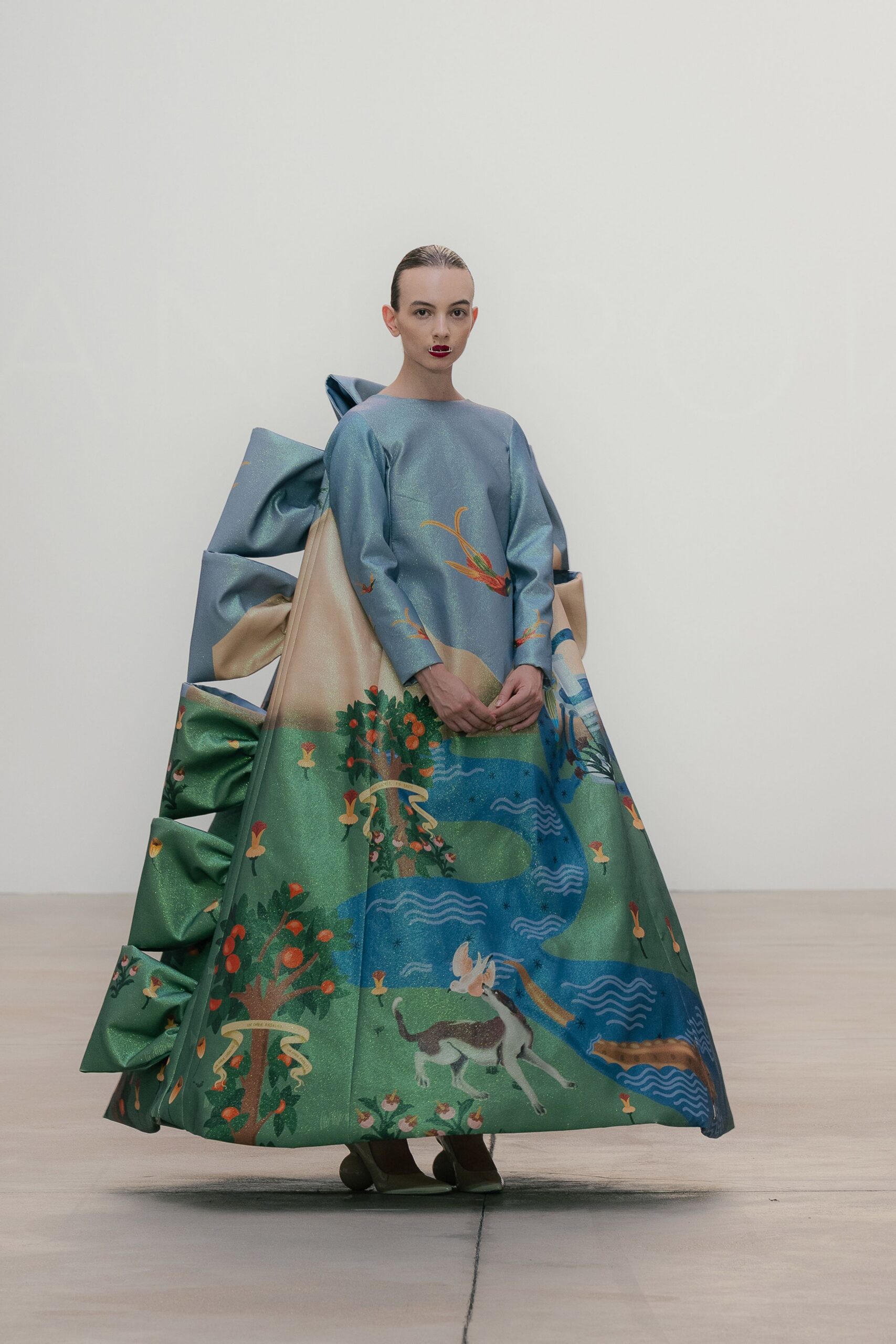 Shimmering sky-blue ballgown printed with a winding river, fruit trees, and a hound. Monumental origami folds rising behind the skirt in stacked sea-green panels. Olive satin pumps peeking from the hem. For the town pageant staged in a museum of local myths.