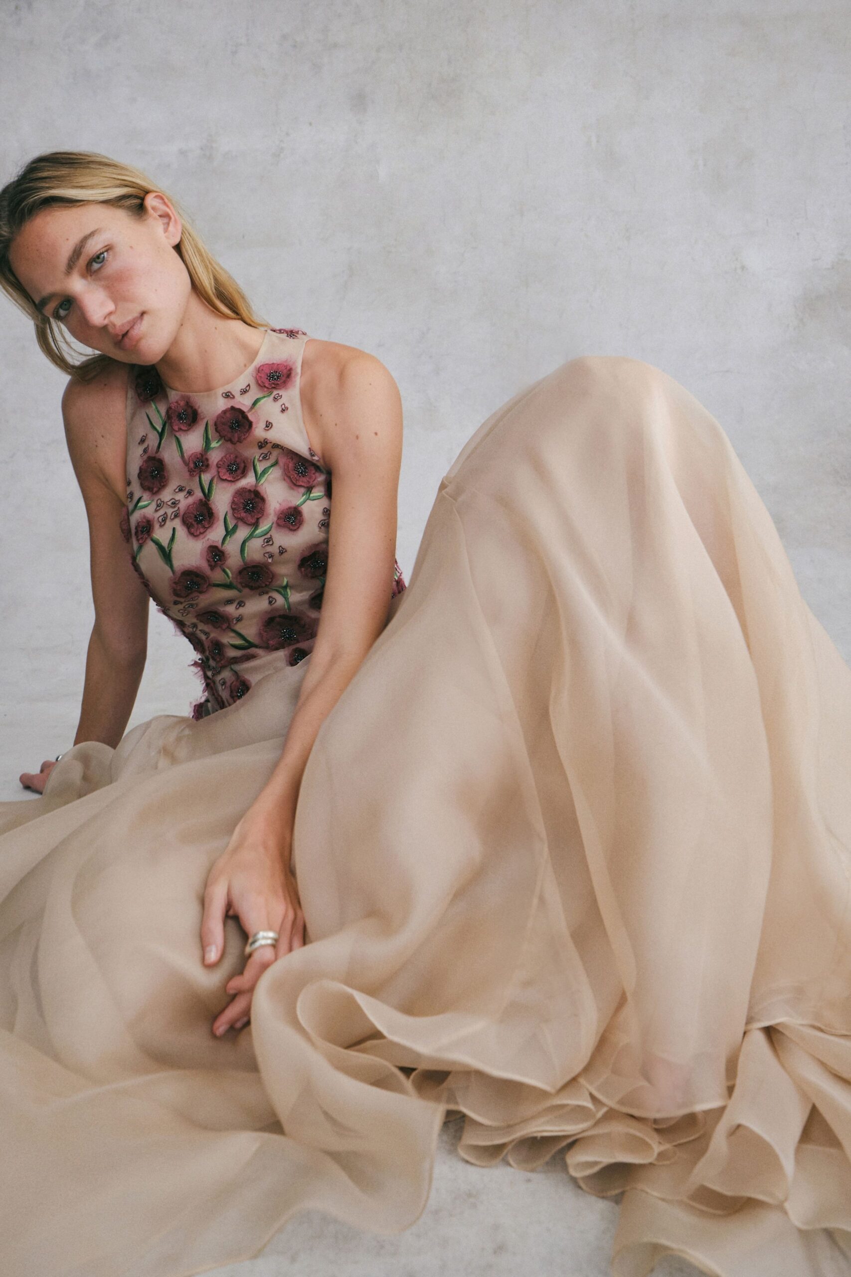 Nude tulle bodice embroidered with plum flowers and green stems. Voluminous champagne organza skirt, hem collapsing into soft folded clouds. Wide silver double band. Afternoon fitting, pins on the floor and someone steaming veils nearby.