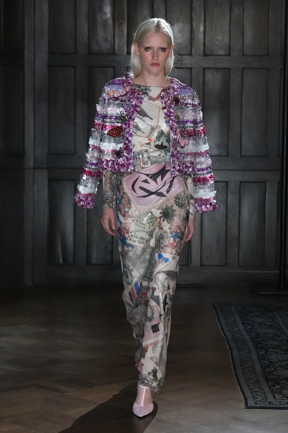 Cropped jacket crusted with lilac and silver paillettes in fuzzy stripes. Printed mesh top, neckline edged with a faint peach seam. Matching sheer sequined trousers with collage prints and a pink wrap panel. Pale pink pumps with a squared throat. Crossing a draughty manor hallway after everyone else has gone upstairs.
