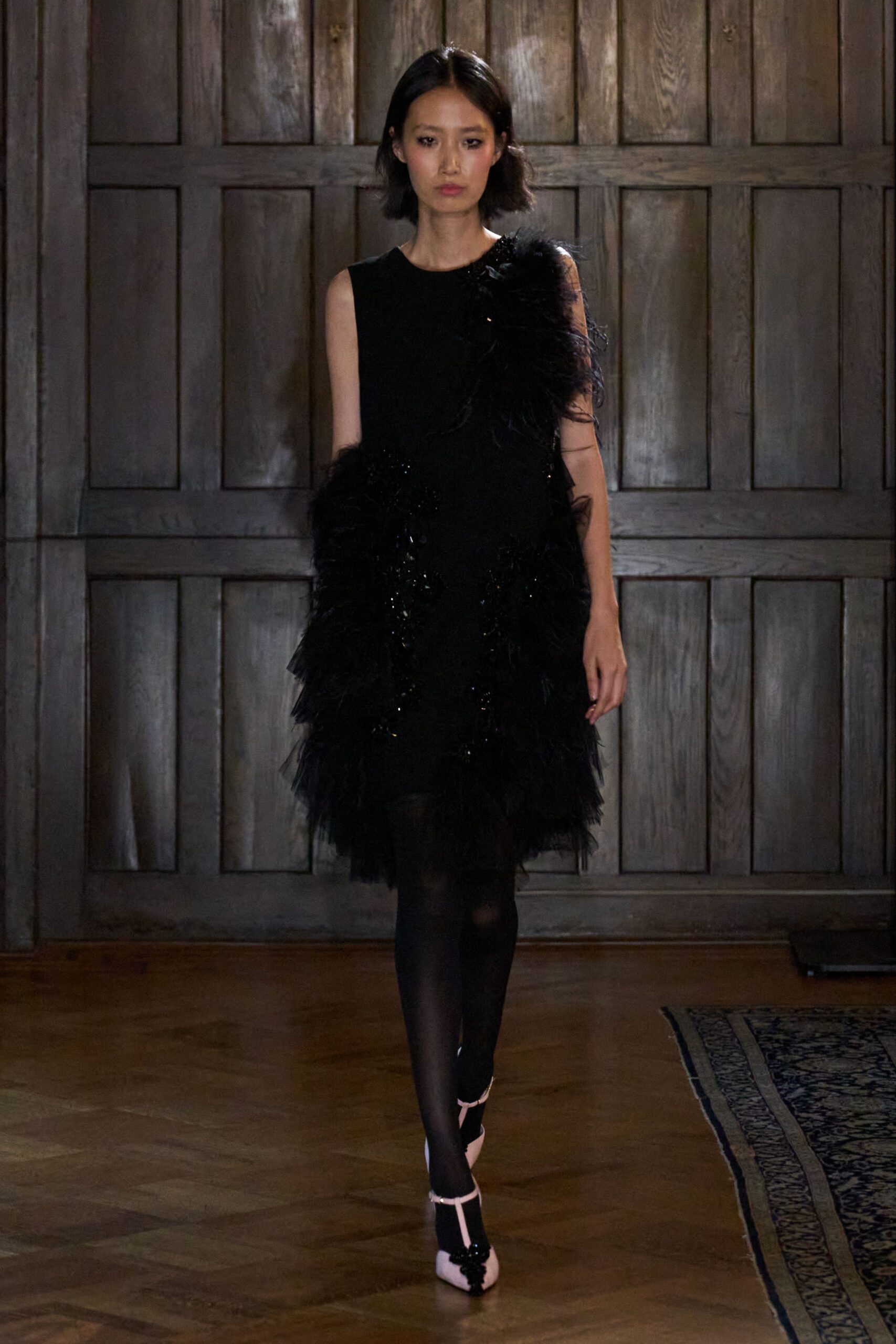 Sleeveless black shift dress, one shoulder and hem engulfed in ostrich-feather tufts. Sheer black tights. Blush Mary Jane pumps with glossy black appliqued toes. Crossing a wood-panelled hotel corridor after the string quartet has packed up.
