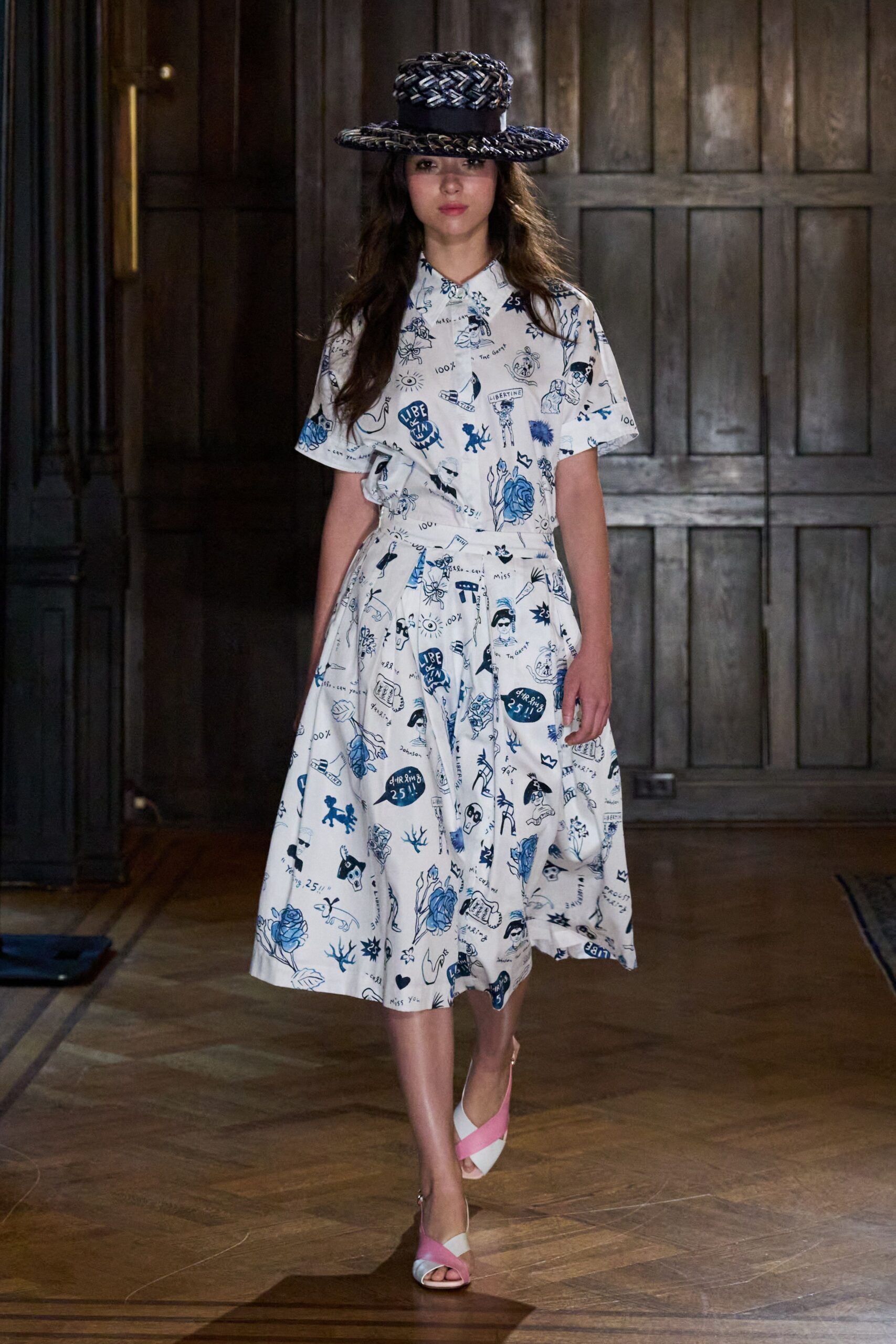 Flat-crowned straw boater woven in navy and cream braid. White shirtwaist midi printed with blue doodles, waist gathered into soft pleats. White satin heels crossed with bubblegum-pink straps. Garden wedding in a paneled country house, thunder holding off till dusk.