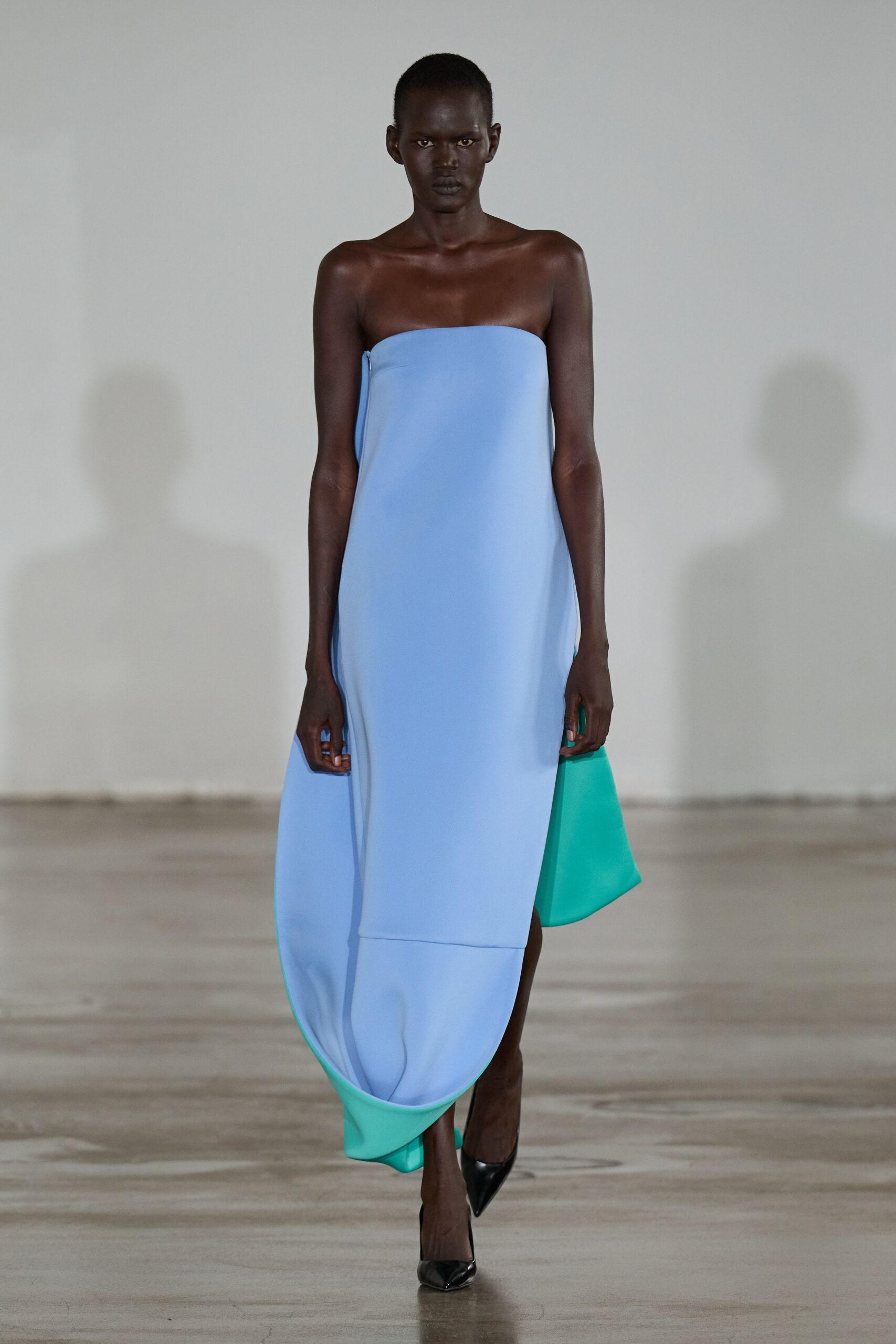Strapless powder-blue column, foam-stiffened hem curling into turquoise scoops. Black patent pumps, sharply pointed. Museum atrium after rain, crossing the floor before the echoes settle.