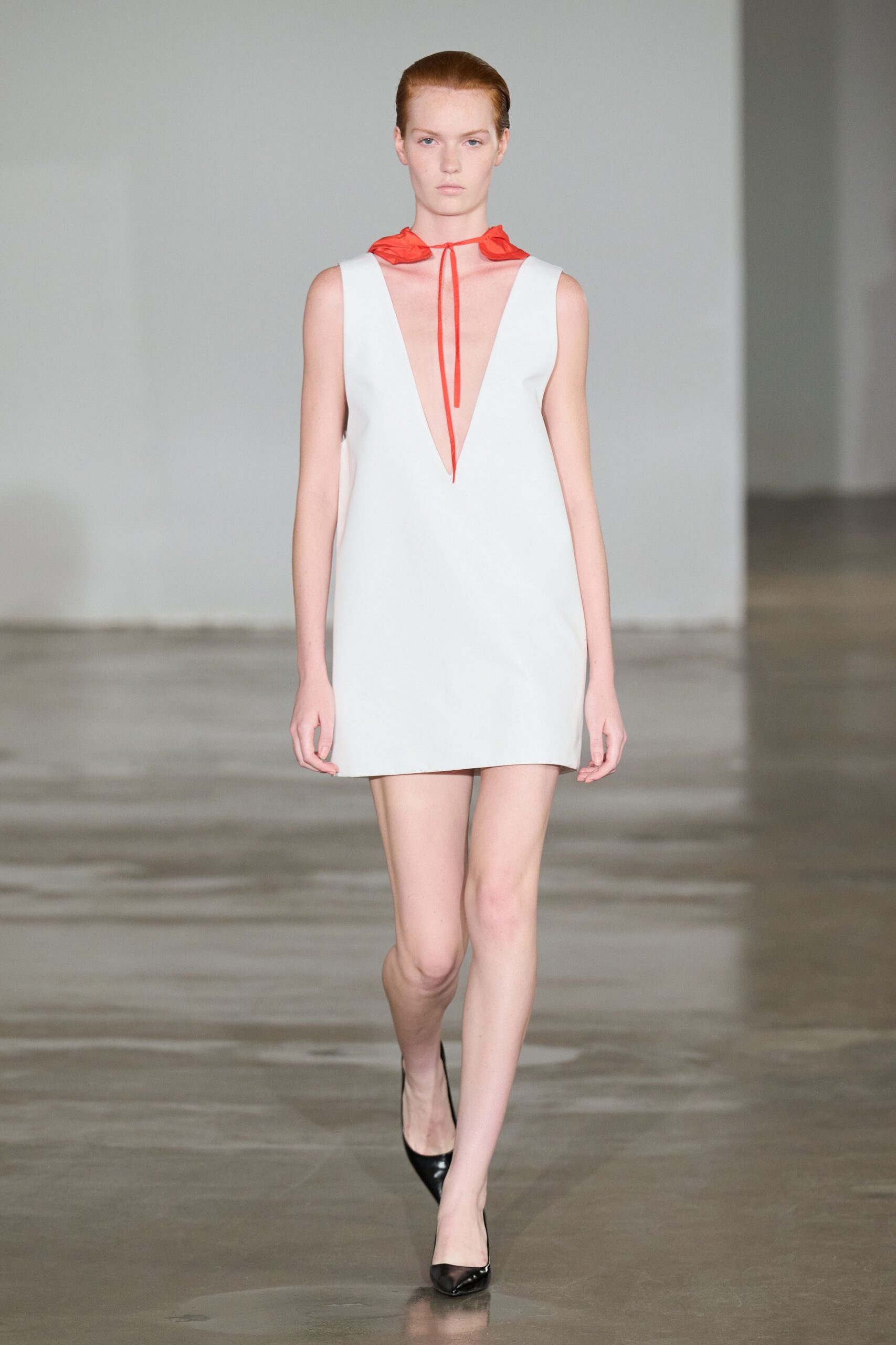 Poppy-red nylon neck scarf tied in a narrow dangling bow. Pale grey mini shift with a plunging V cut nearly to the waist. Black patent pointed pumps. For opening a hotel room balcony door just before the storm breaks.