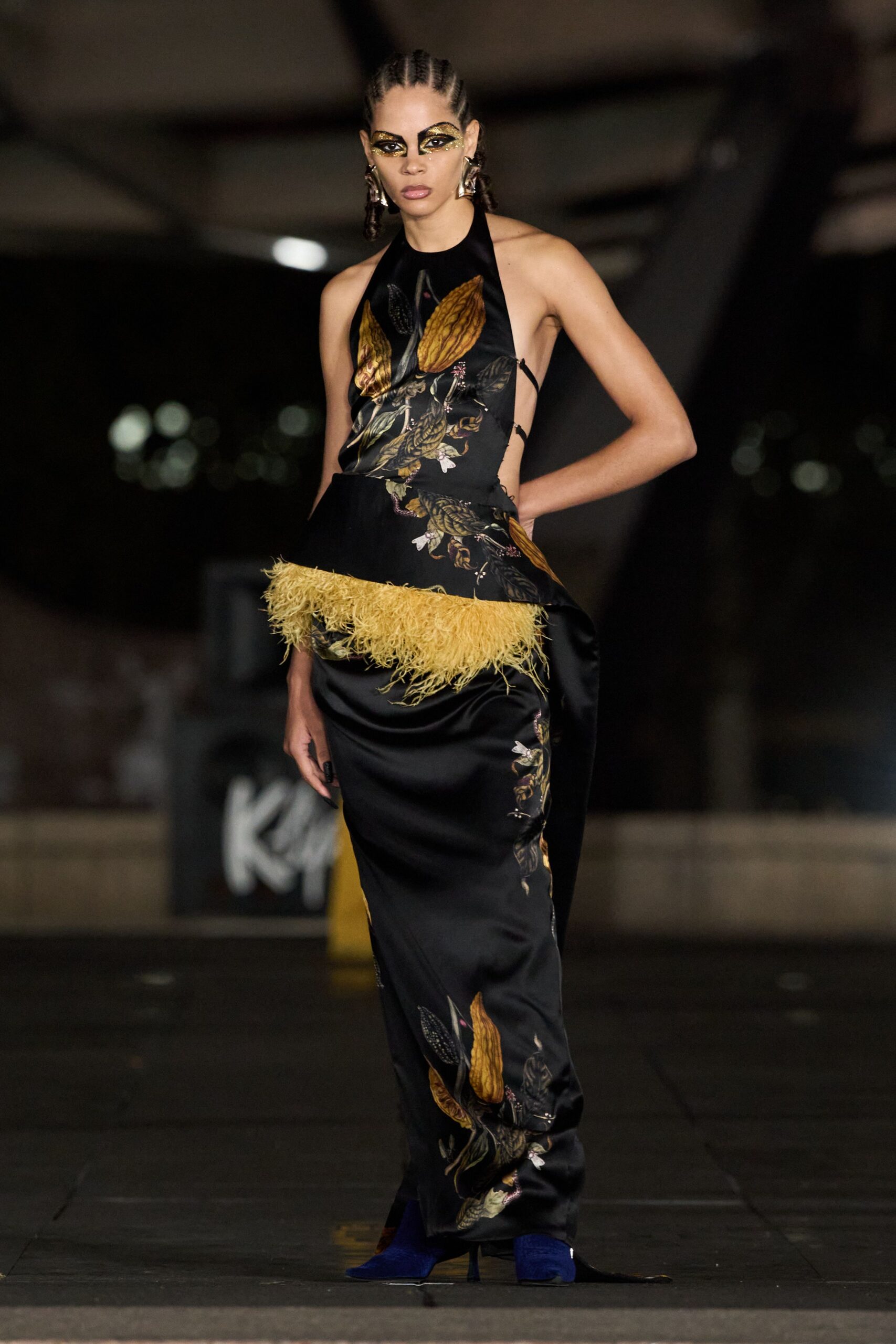 Crumpled silver drop earrings. Black satin halter gown with botanical print and mustard feather peplum. Cobalt velvet pointed boots peeking under the hem. Crossing a hotel forecourt after midnight with petals stuck to your shoes.