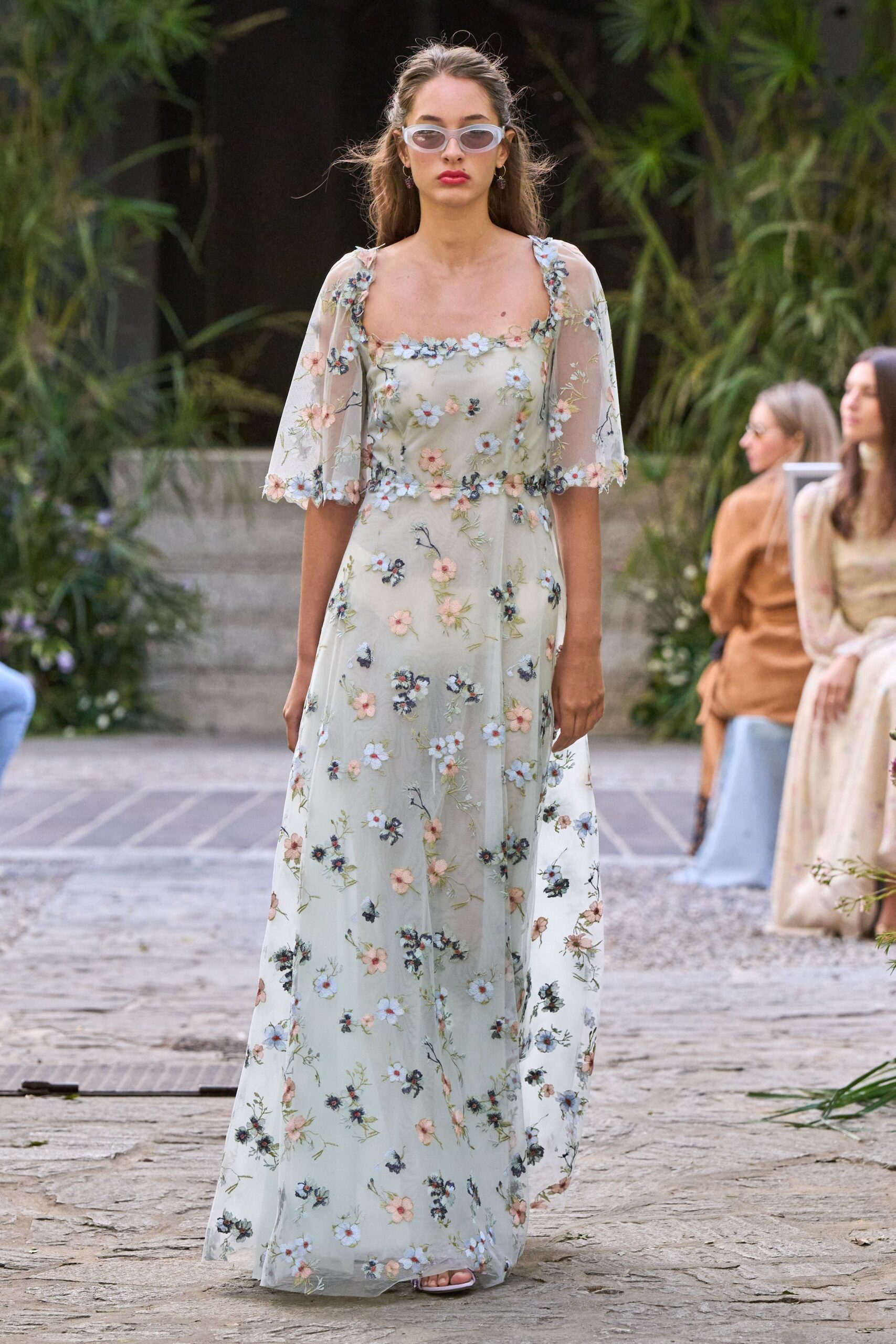 Milky oval sunglasses with narrow smoke lenses. Pale celadon tulle gown, scattered with appliqued blossoms and flutter sleeves. Barely there white sandals peeking from the hem. Walking through a garden courtyard after the heat finally breaks.