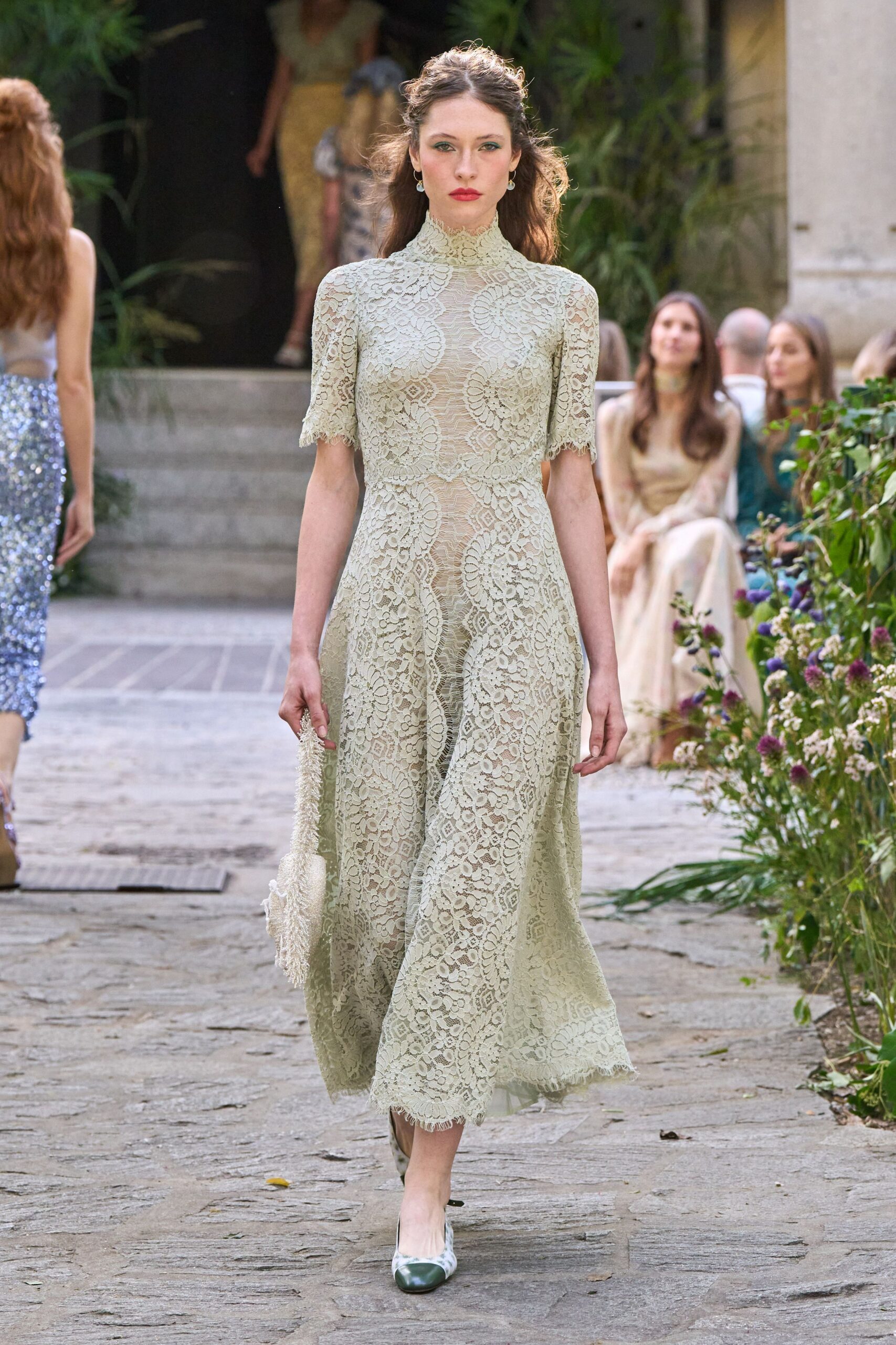Pale sage corded lace dress with a high neck and eyelash cuffs. Ivory beaded fringe bag hanging limp from one hand. Pale pumps with dark cap toes. Crossing a cloister courtyard after the wedding guests have found shade.