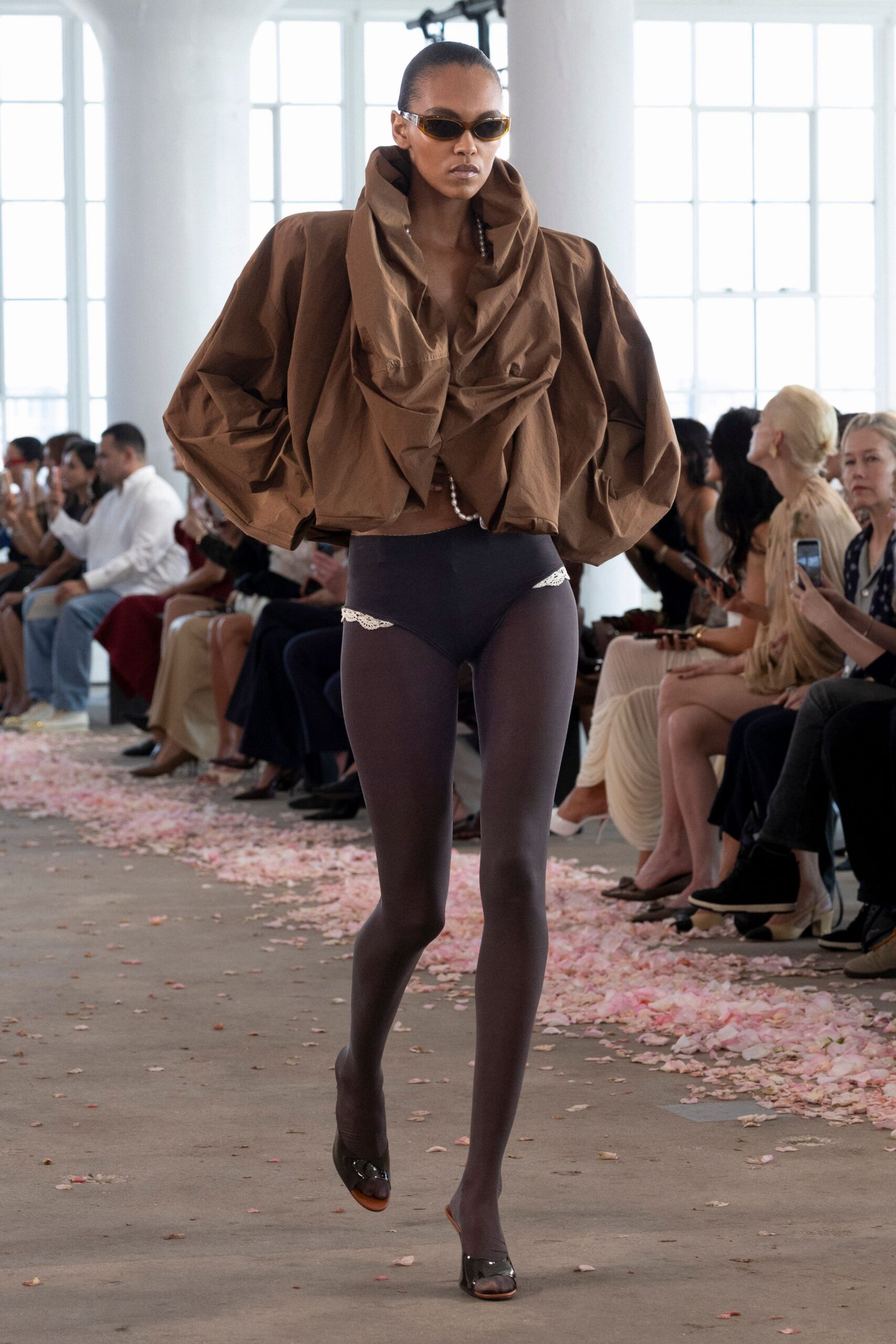 Amber wraparound sunglasses with narrow pointed frames. Chocolate taffeta blouse, collar collapsing into a deep crumpled cowl. High-cut black briefs with white lace peeking at each hip. Smoke sheer tights. Black patent peep-toe mules. Crossing a conservatory floor after the wedding petals have gone limp.