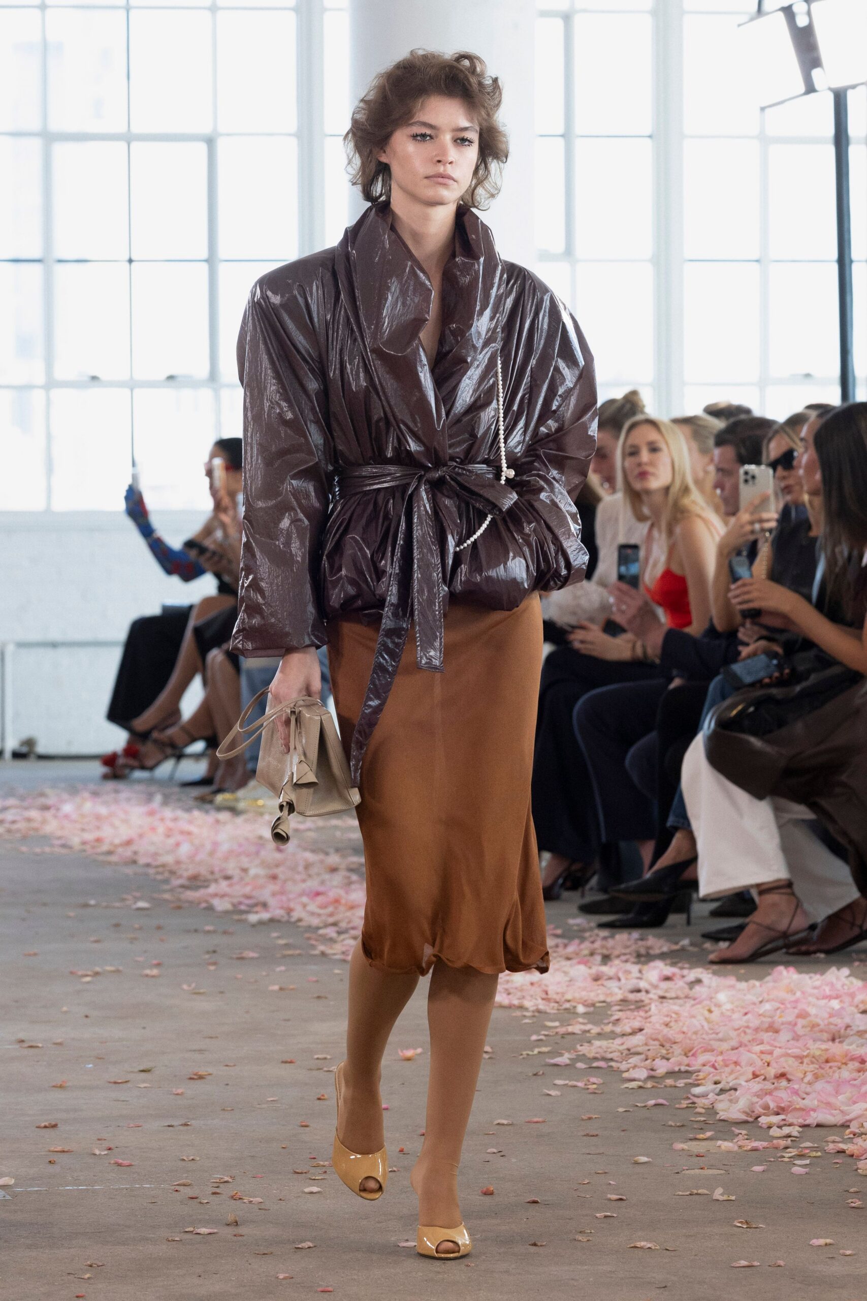 Glossy aubergine shell wrap jacket, blown collar and long self-tie belt. Caramel bias-cut skirt with a softly rolling hem. Sheer tan tights. Crumpled beige clutch with a looped wrist strap. Nude patent peep-toes. Walking home from a benefit lunch with petals stuck to your soles.